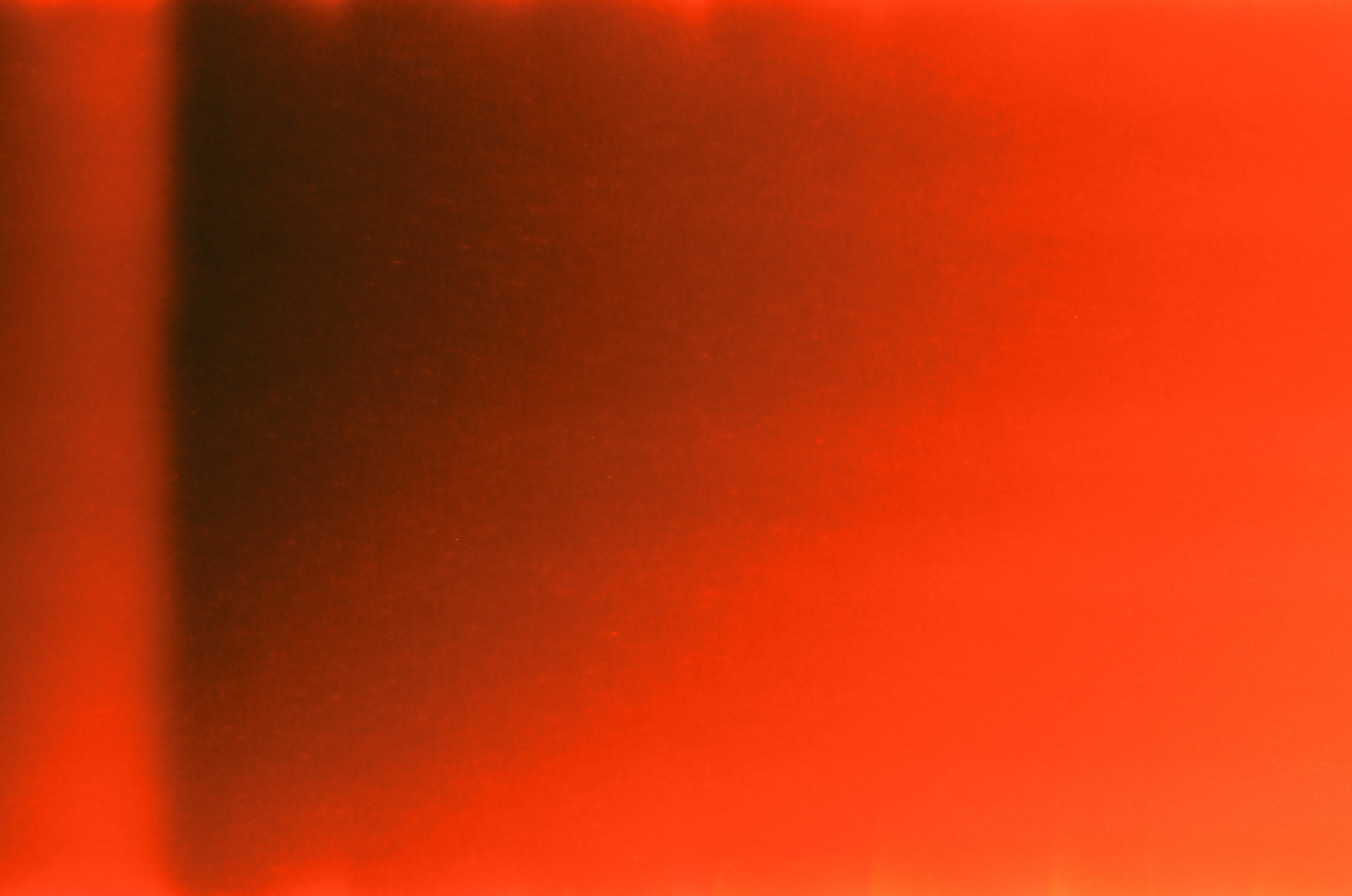 A fully light-struck film frame showing a gradient of bright red and orange with a dark burned area on the left side.