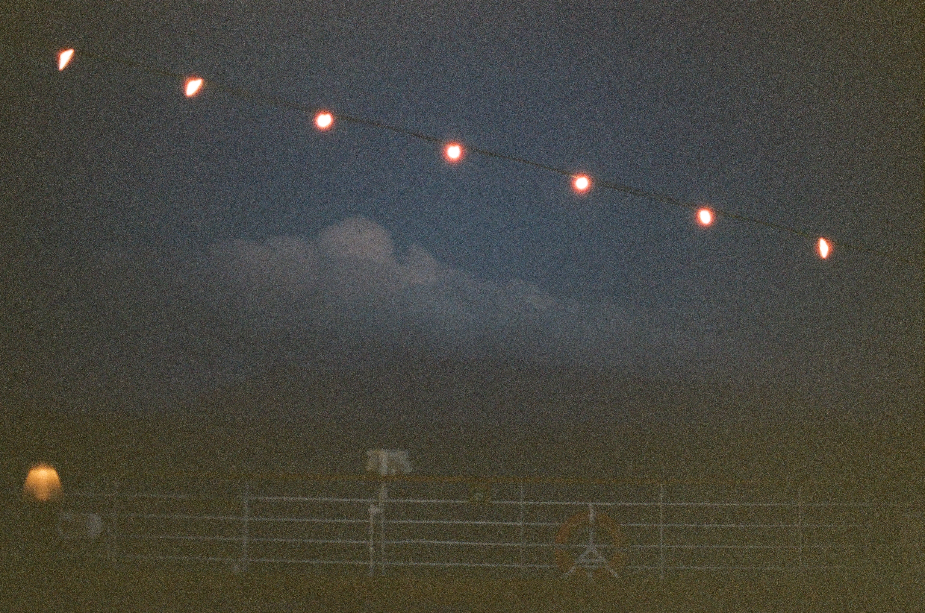 A curved row of warm bulbs hangs above a dark railing with cloud-wrapped mountains faintly visible beyond.
