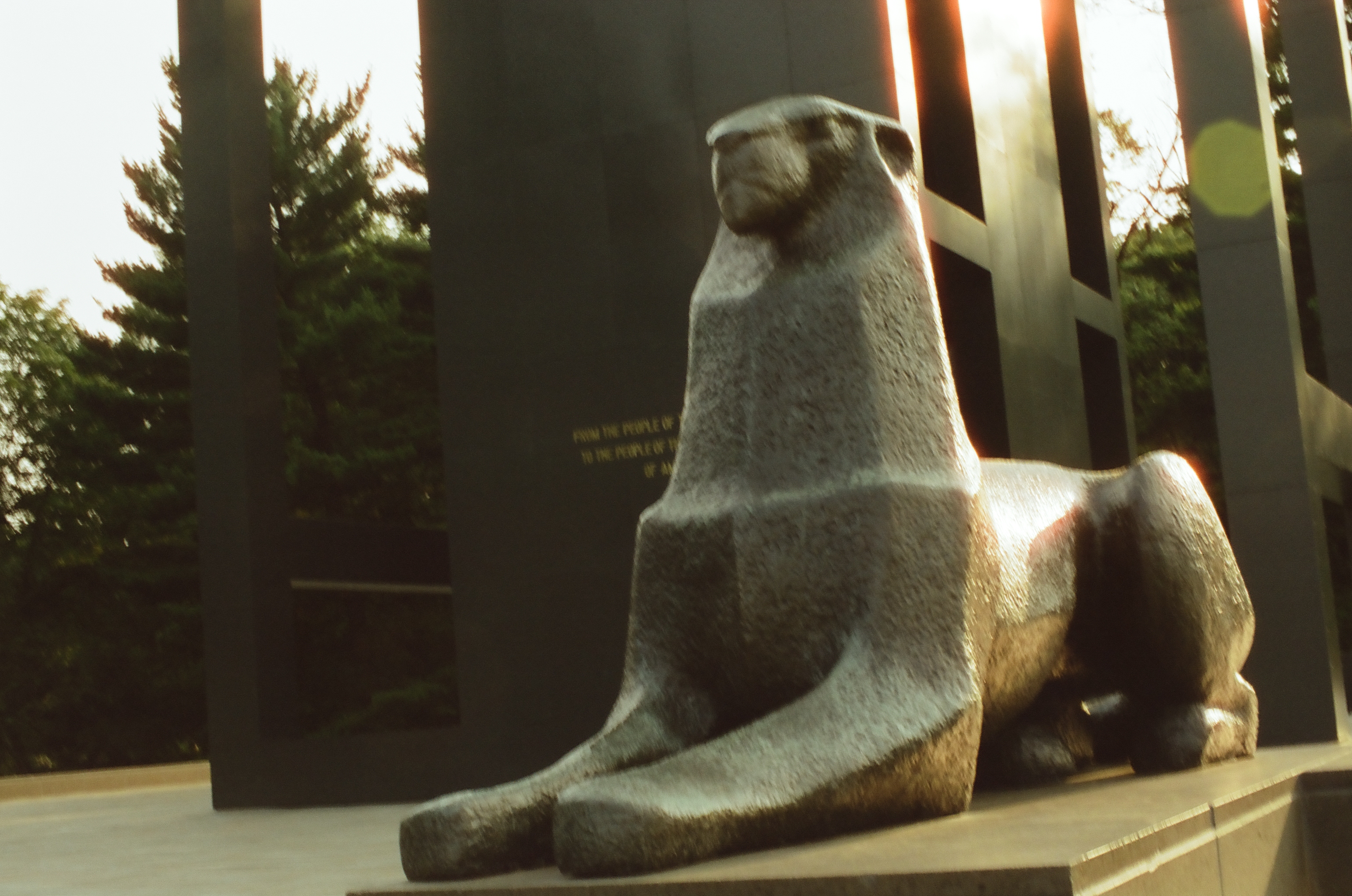 A seated stone animal sculpture catches warm side light beside dark vertical metal elements.