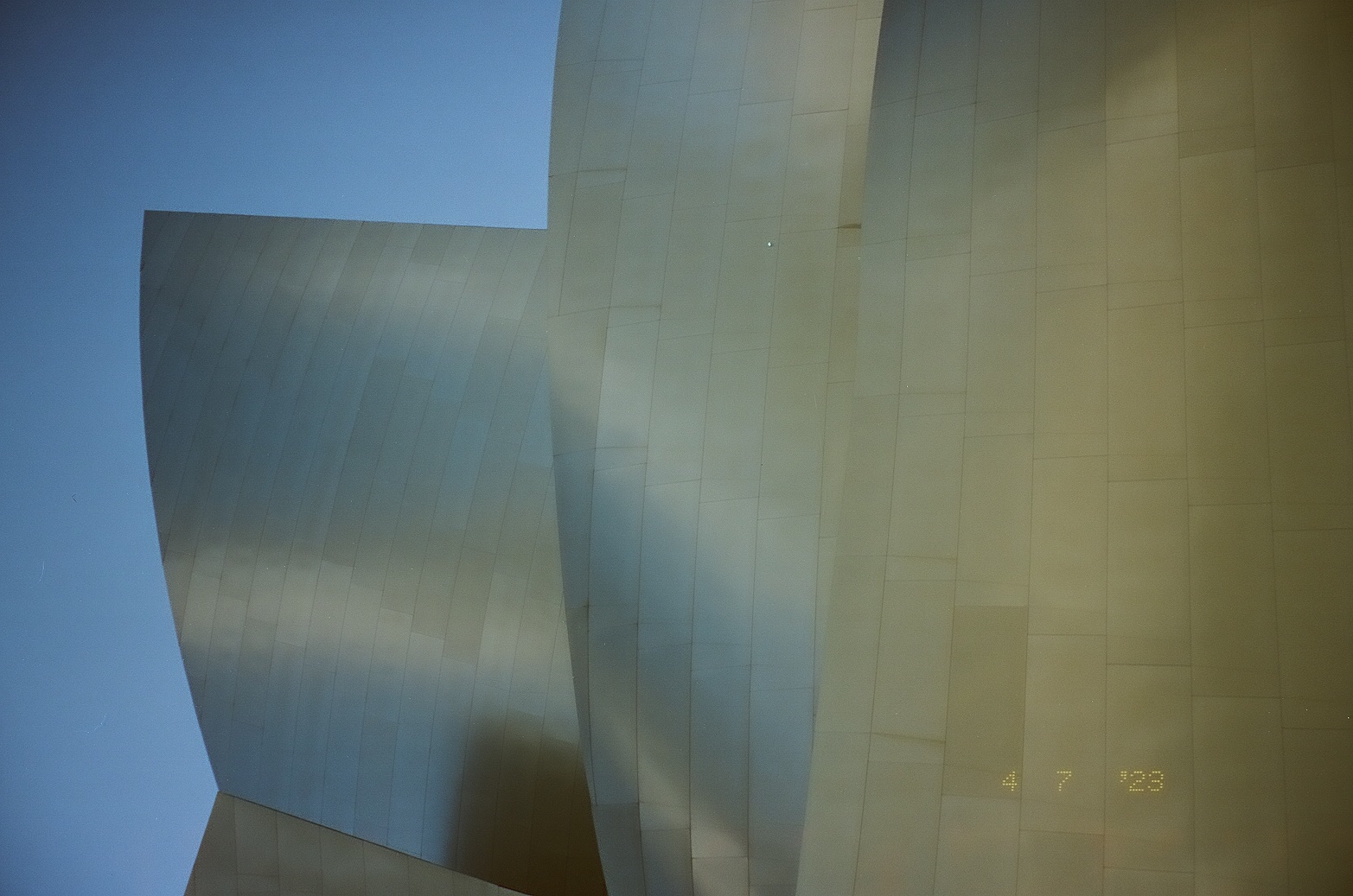 A rounded metal volume rises above a lower curved wall beneath clear blue daylight.