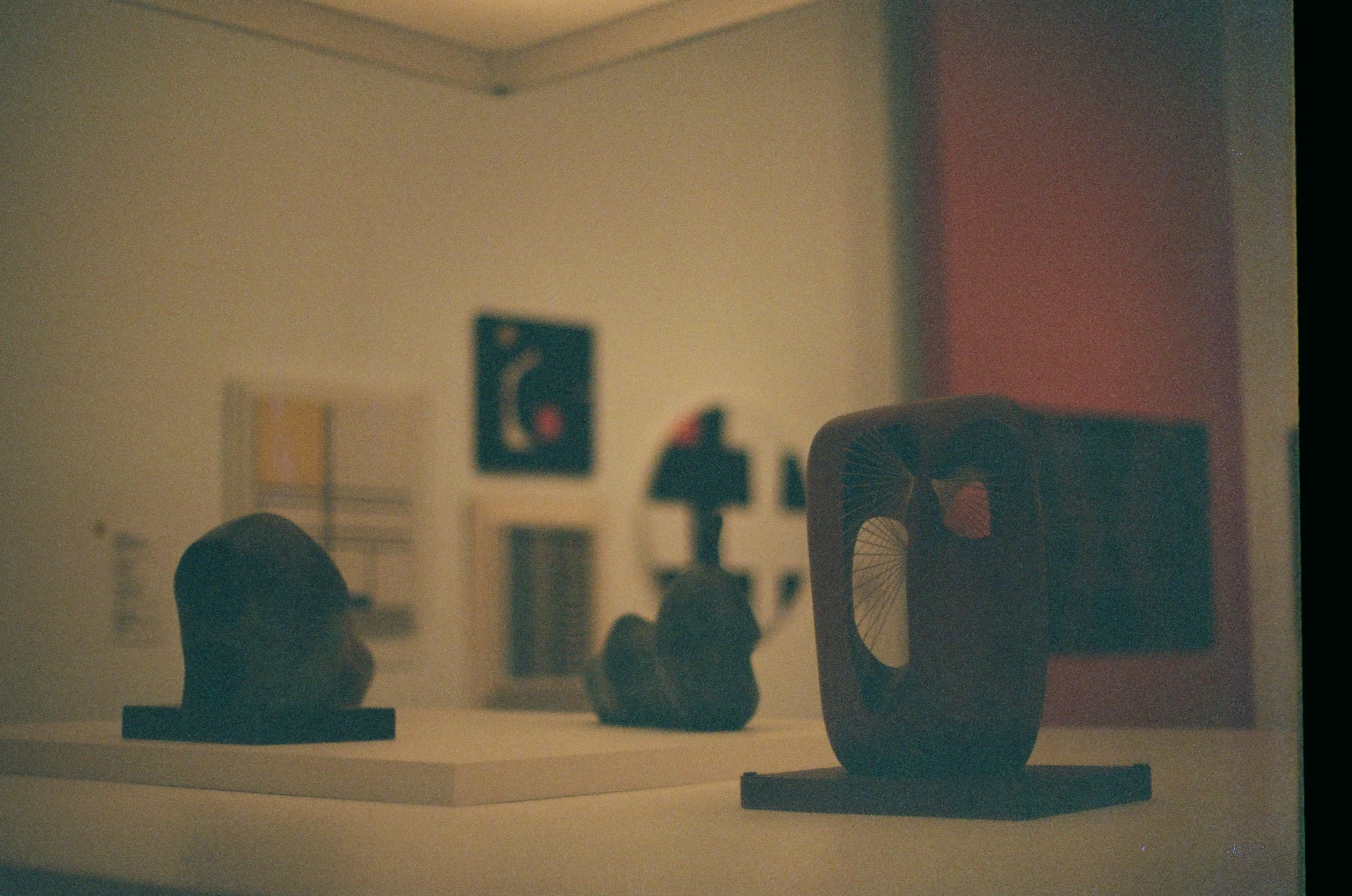 Several dark abstract forms sit on pale gallery plinths beneath soft warm interior light.