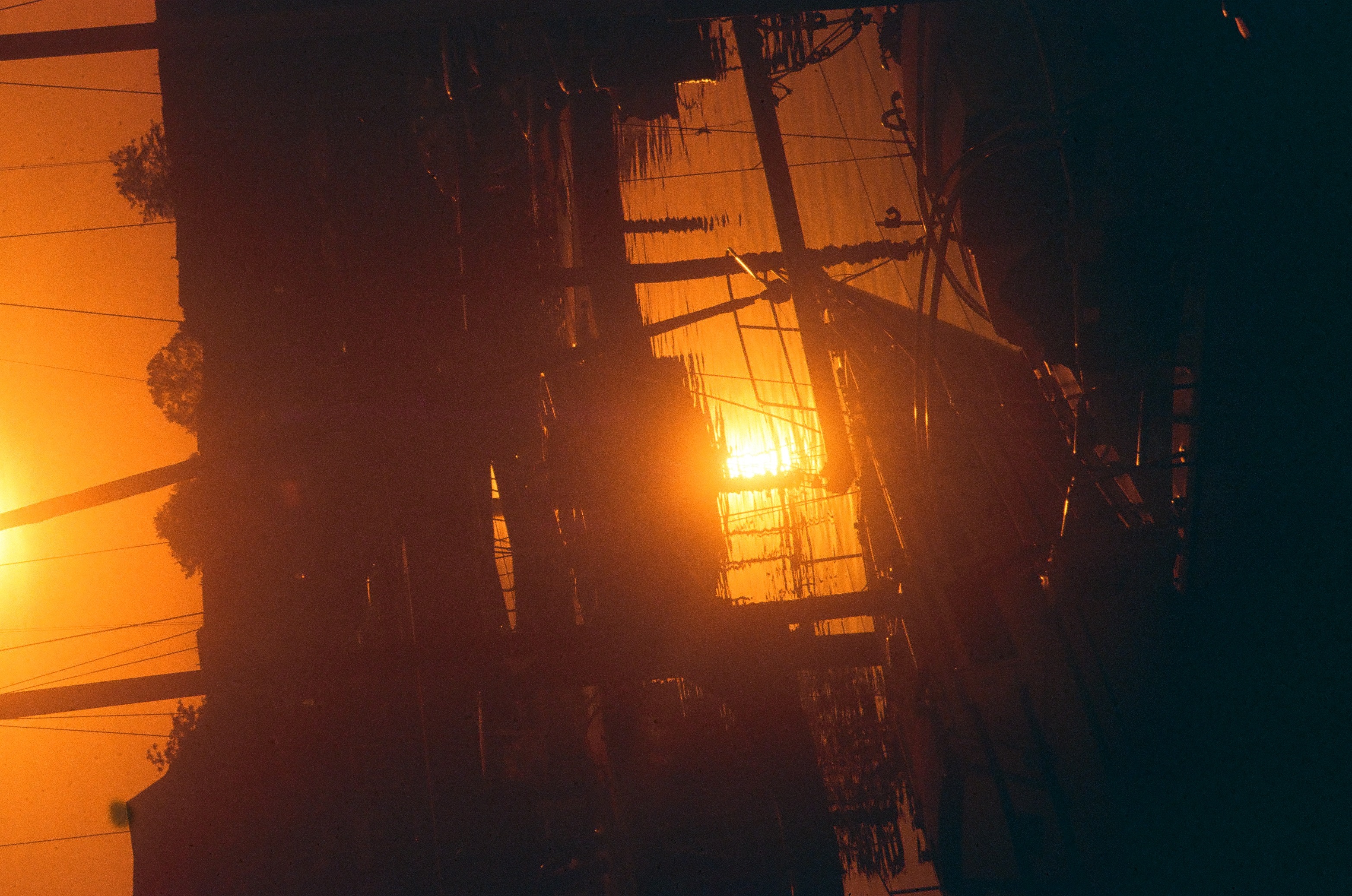 A dark utility pole strung with wires stands before a diffuse orange glow, its silhouette doubled by streaking light leaks.