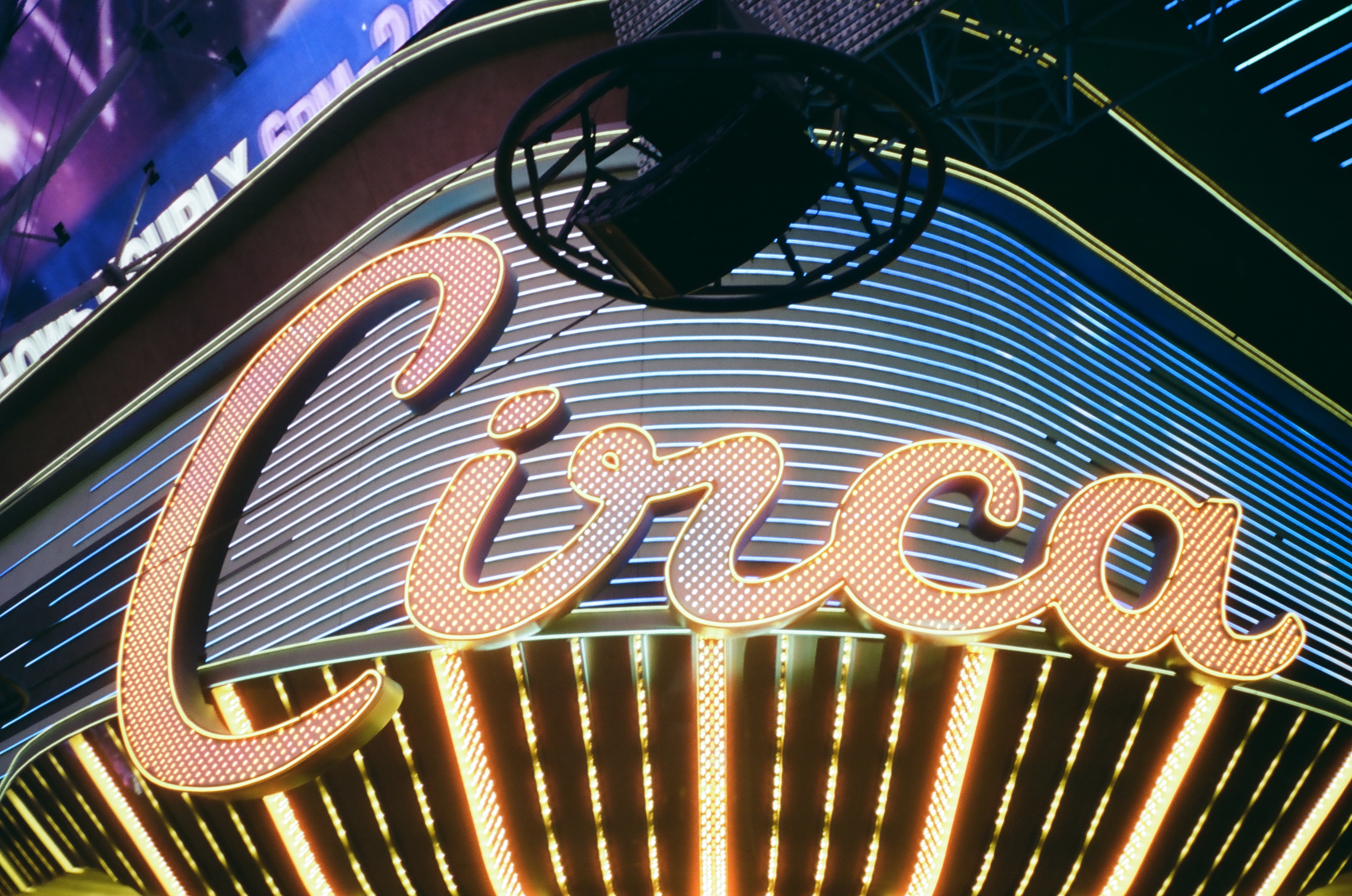 Cursive neon letters spelling Circa glow in warm bulbs above ribbed blue tube lighting, with another sign's edge visible in the corner.