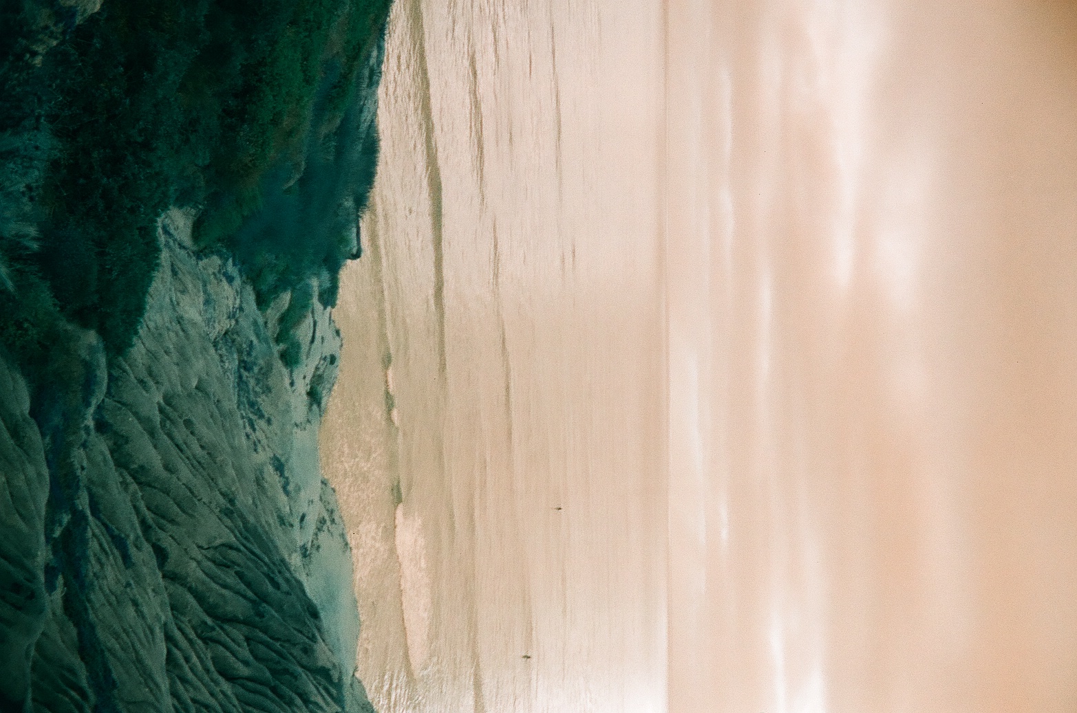 A calm pale ocean extends beyond deeply colored eroded rocks under a softly layered sky.