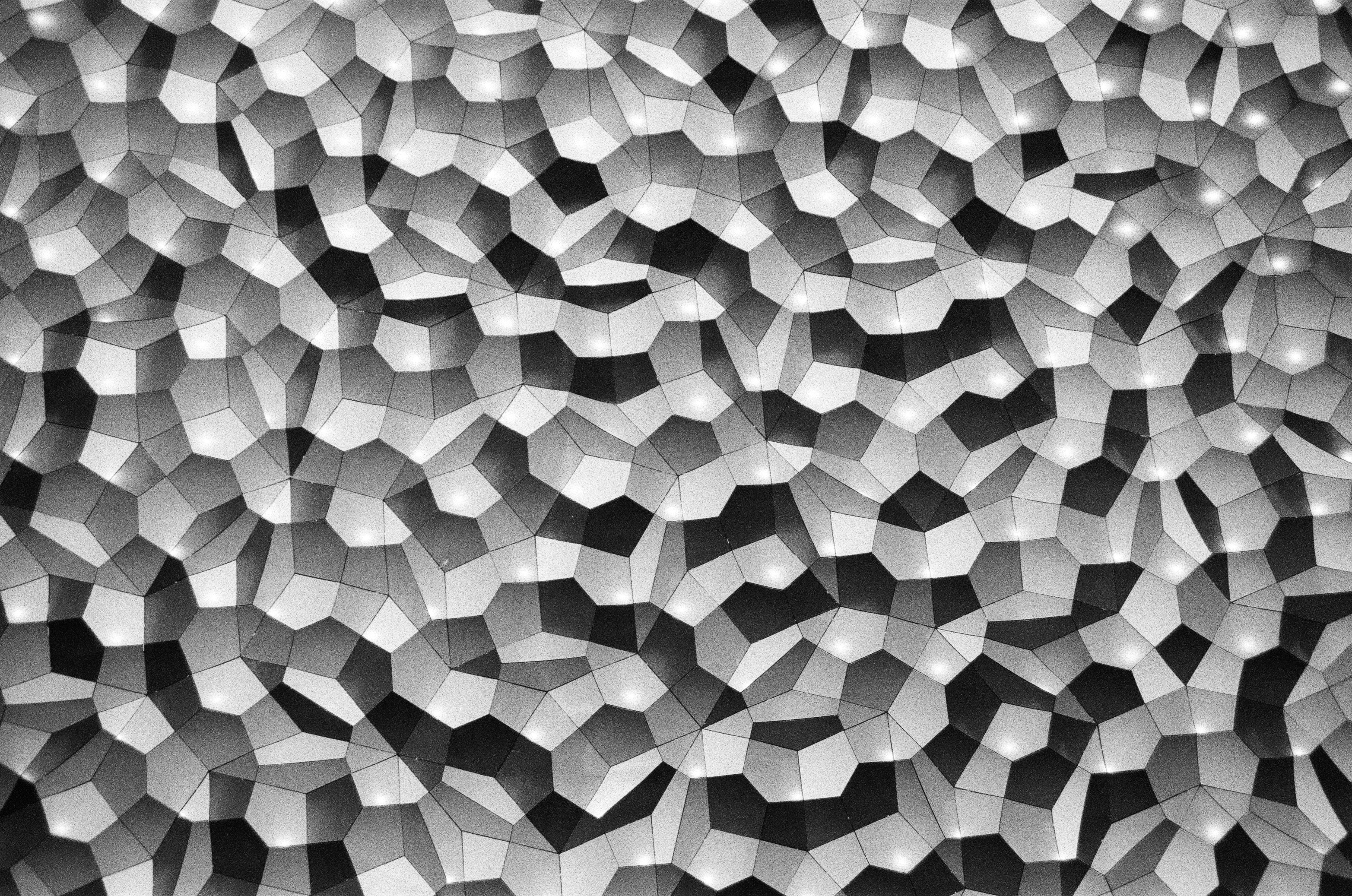 A close view of raised polygonal wall tiles creates a continuous field of gray peaks and black creases.