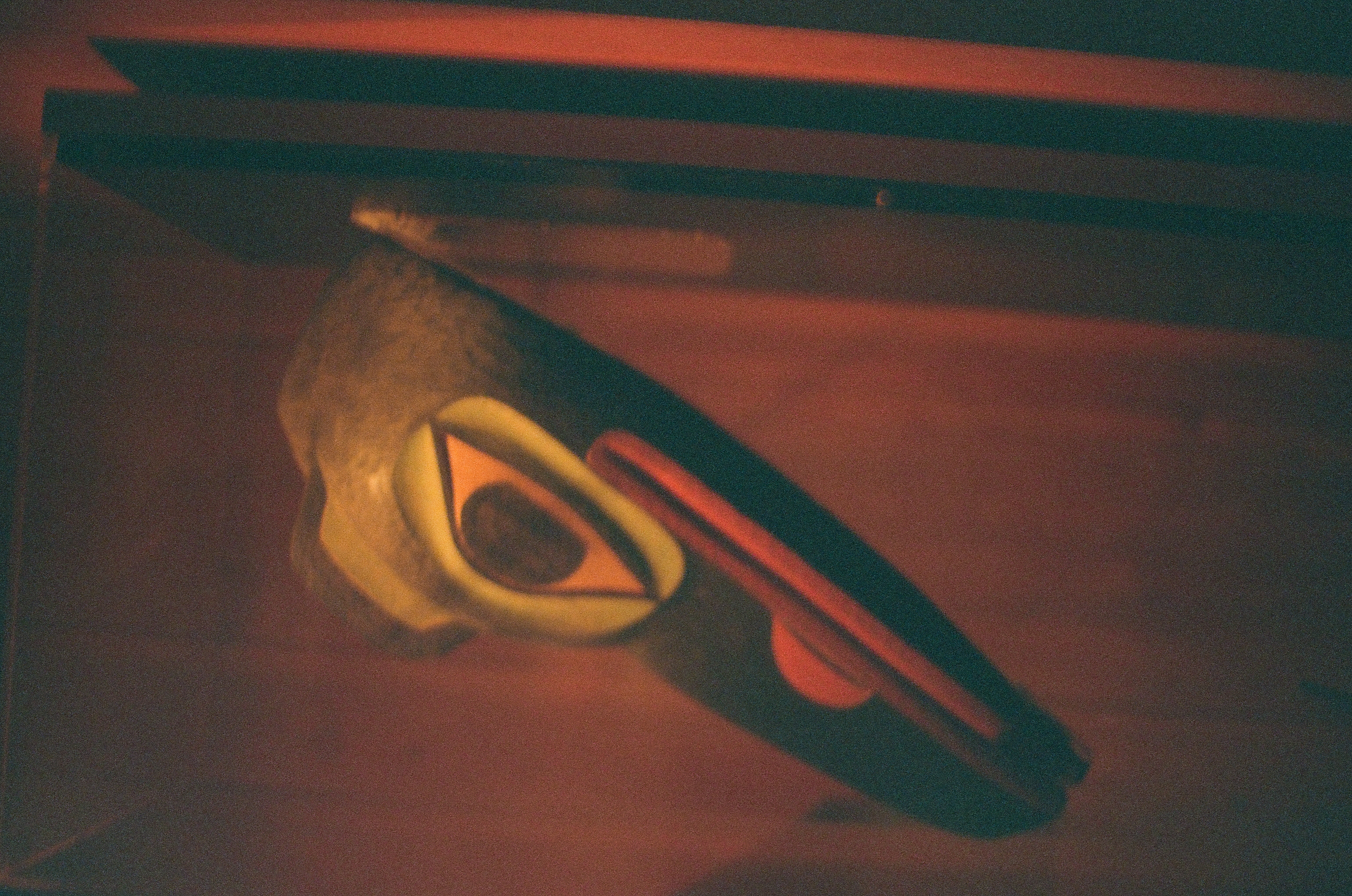 A small painted wooden mask projects from a dark red wall beneath a warm interior light.