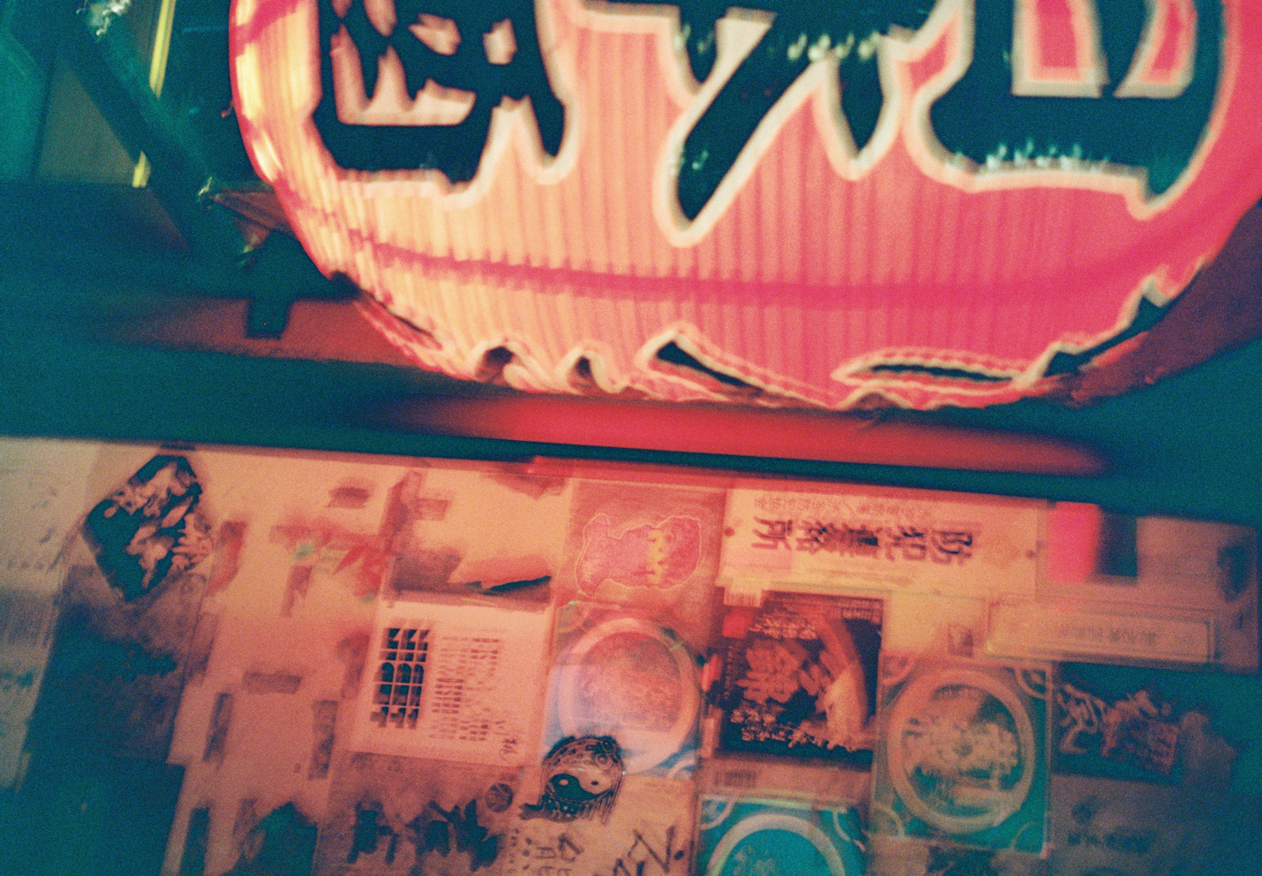 A red paper lantern printed with dark characters glows beside a wall covered in overlapping stickers, notices, and pasted paper.