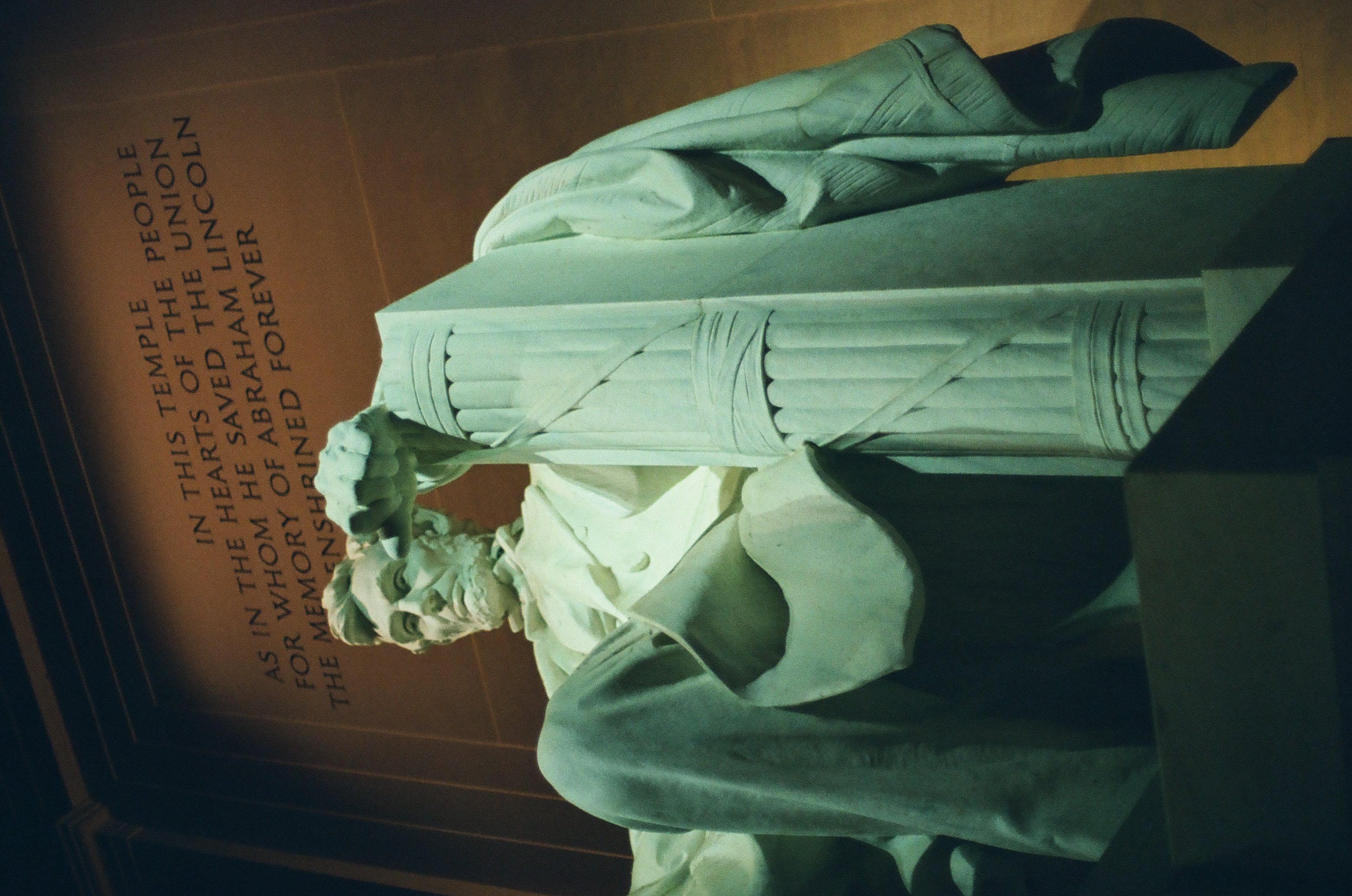 A large seated stone figure rises beneath an engraved wall inscription in a dark, dramatically lit interior.