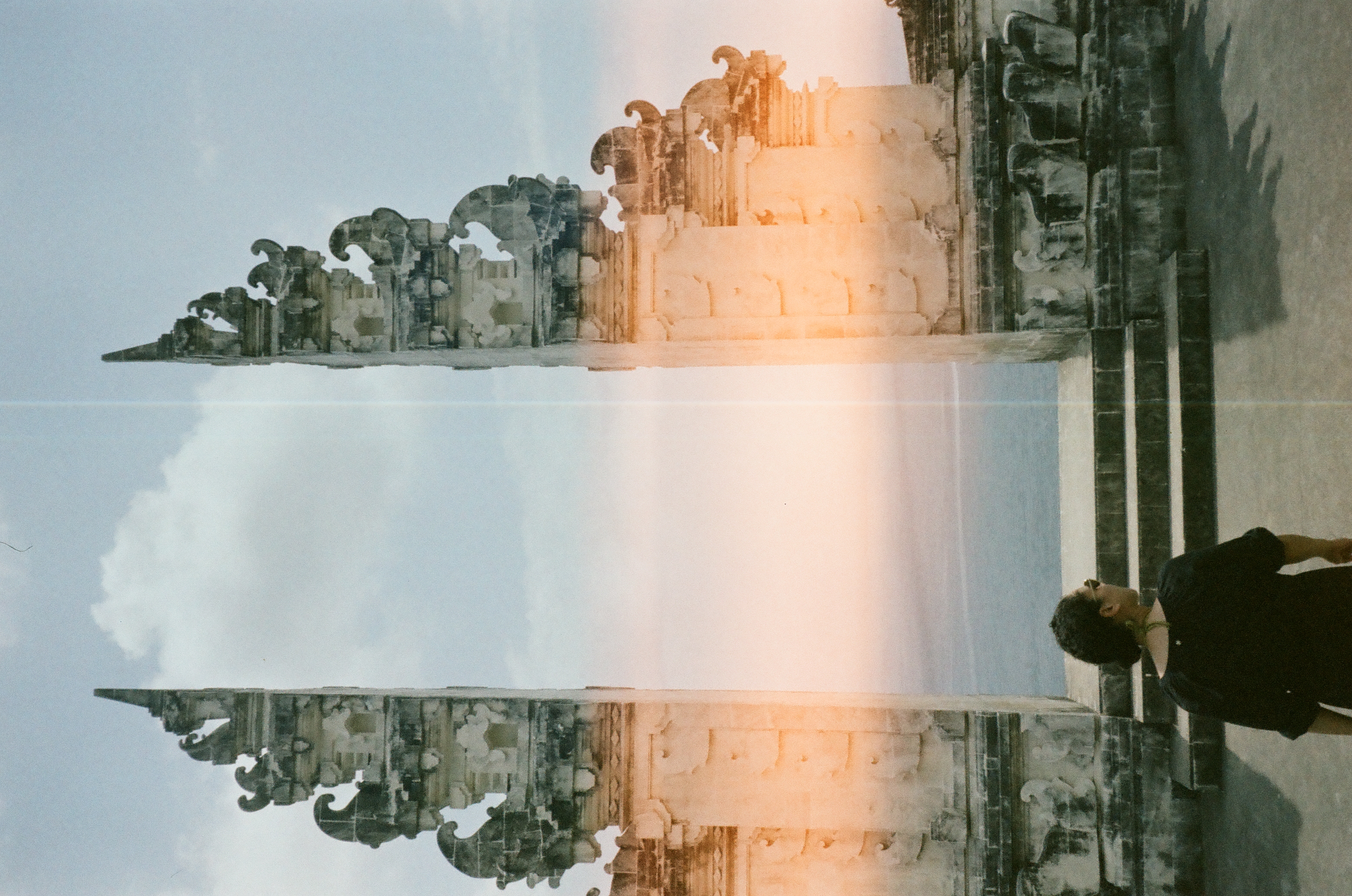 A person in black stands before centered steps between ornate stone towers, crossed near the middle by a pale vertical line.