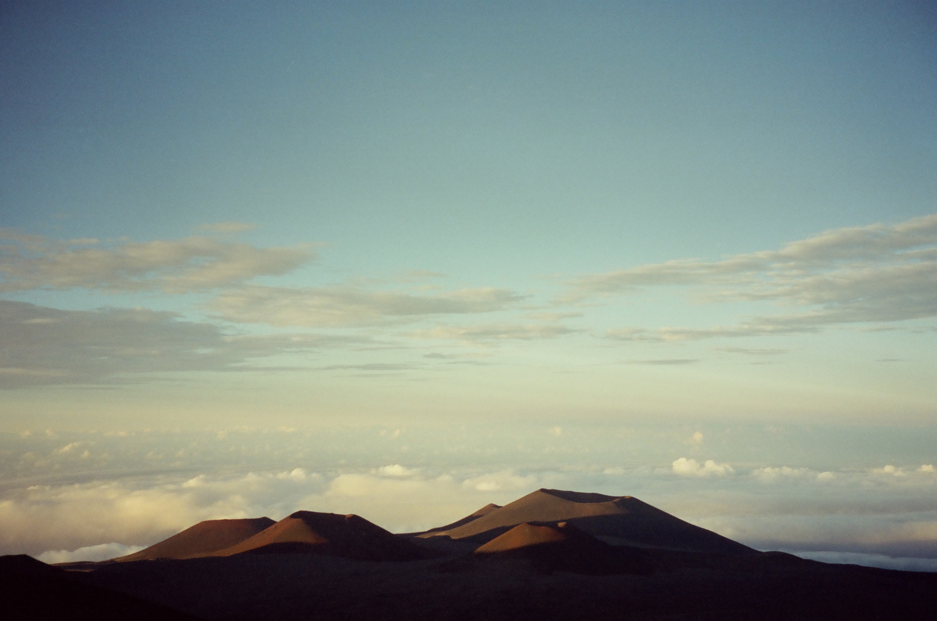 A line of dark volcanic cones breaks the horizon above a distant white cloud deck.