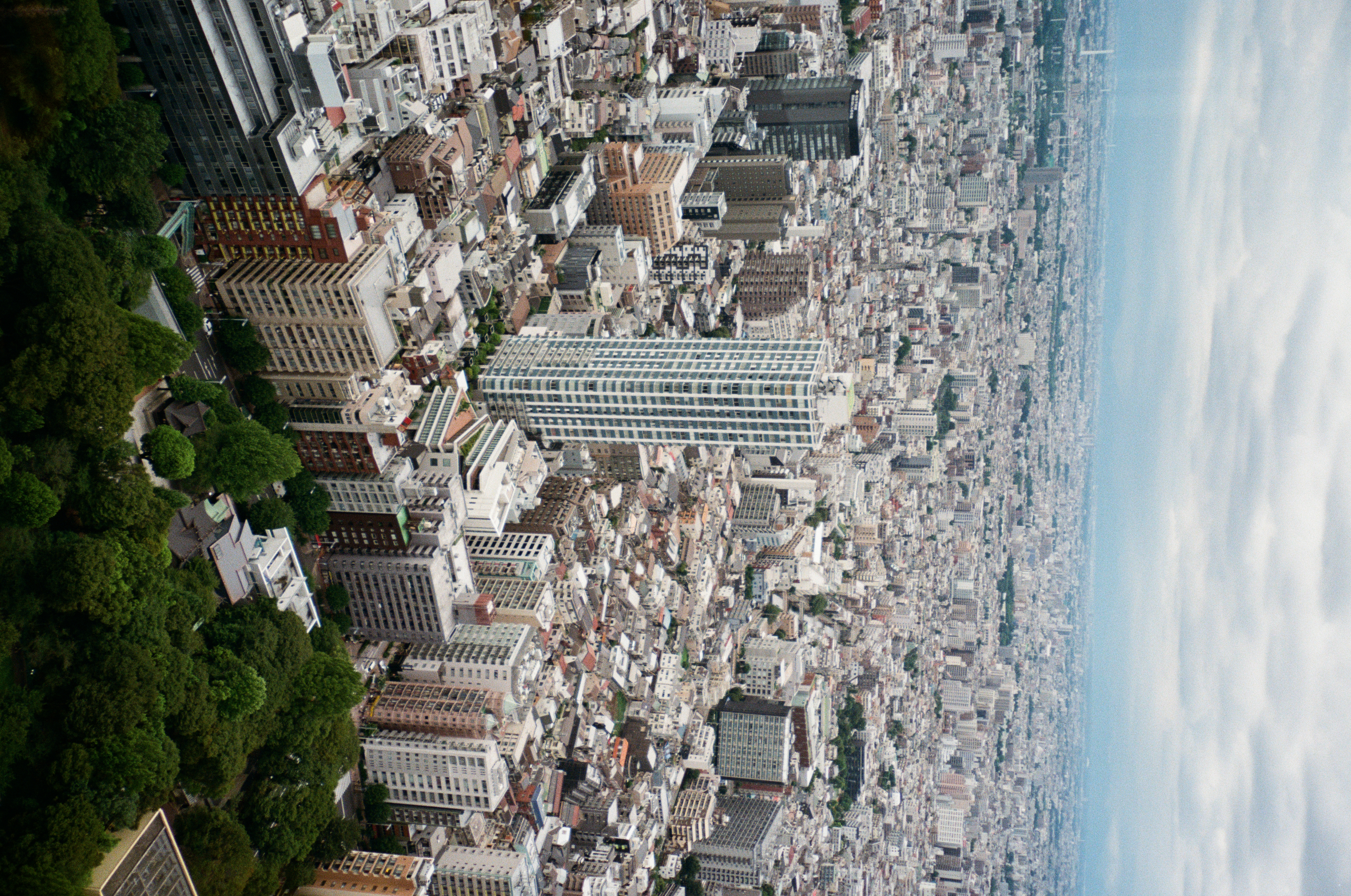 A slender white tower stands apart from a dense, unbroken sprawl of low buildings that runs to a hazy horizon under cloud.