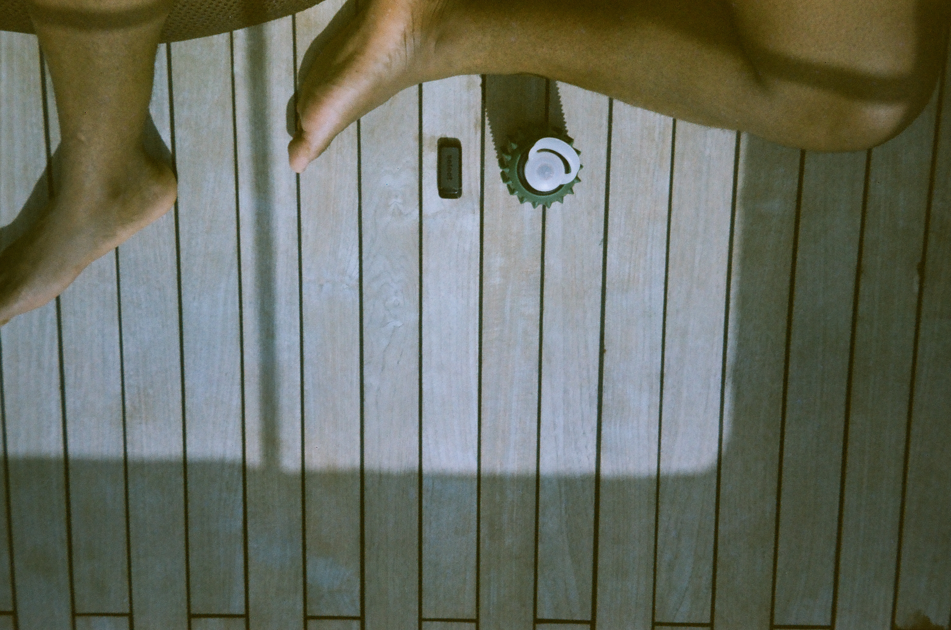 Bare legs and feet cross a pale slatted deck around an unidentified dark elongated object with a round pale end.