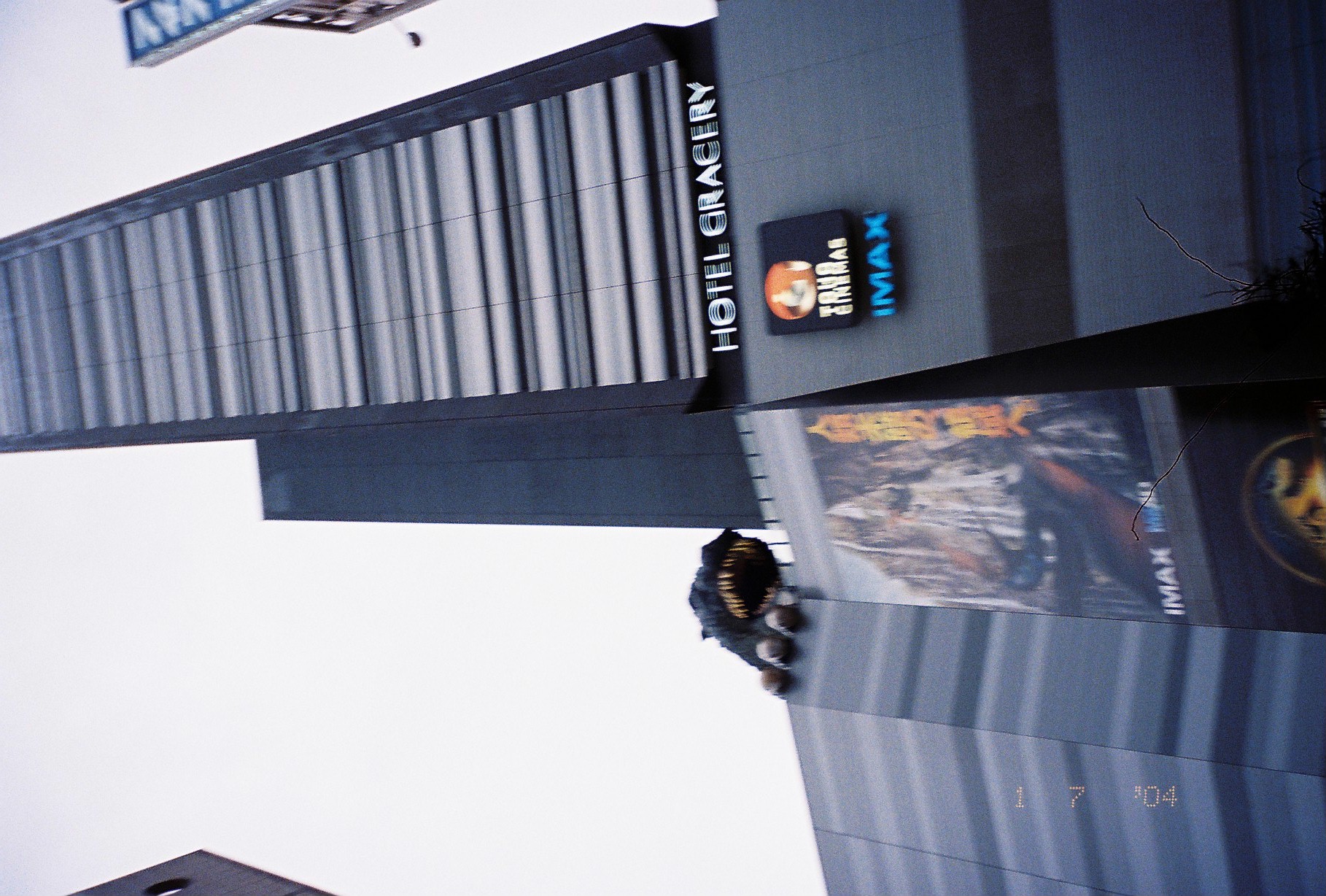 A tall striped building reads 'HOTEL GRACERY' with 'TOHO CINEMAS' and 'IMAX' signage below, while a sculpted creature head peers over a ledge partway up.