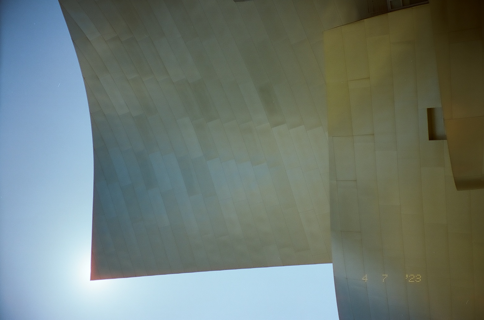 Bright sun catches the upper edge of a tall curved metal wall against deep blue sky.