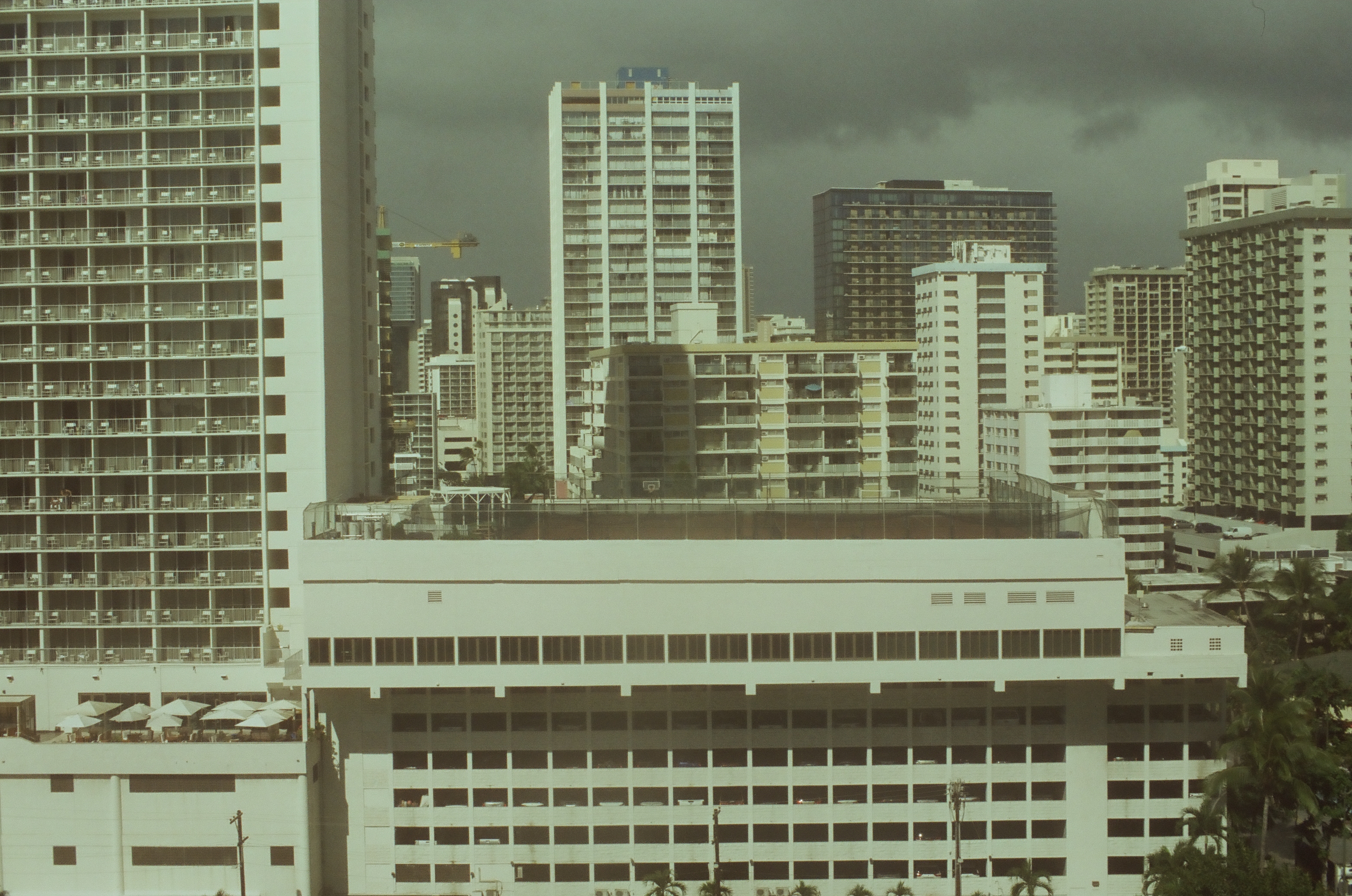 Dense cream-colored high-rise towers with a construction crane crowd together beneath a heavy, storm-darkened gray sky.