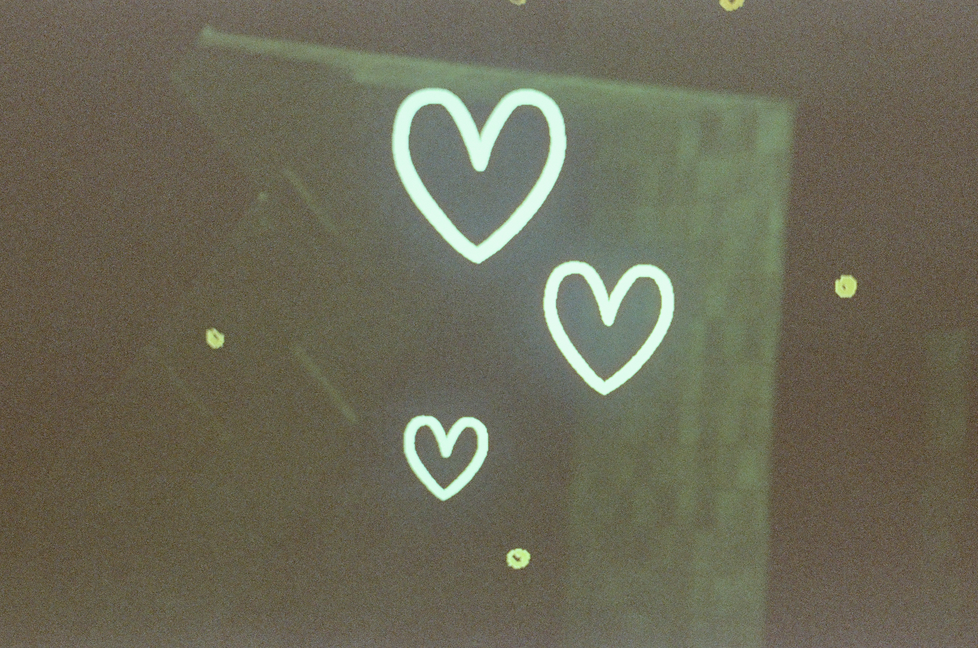 Three glowing white heart outlines of different sizes float against a dark green-brown surface with small scattered light flecks.