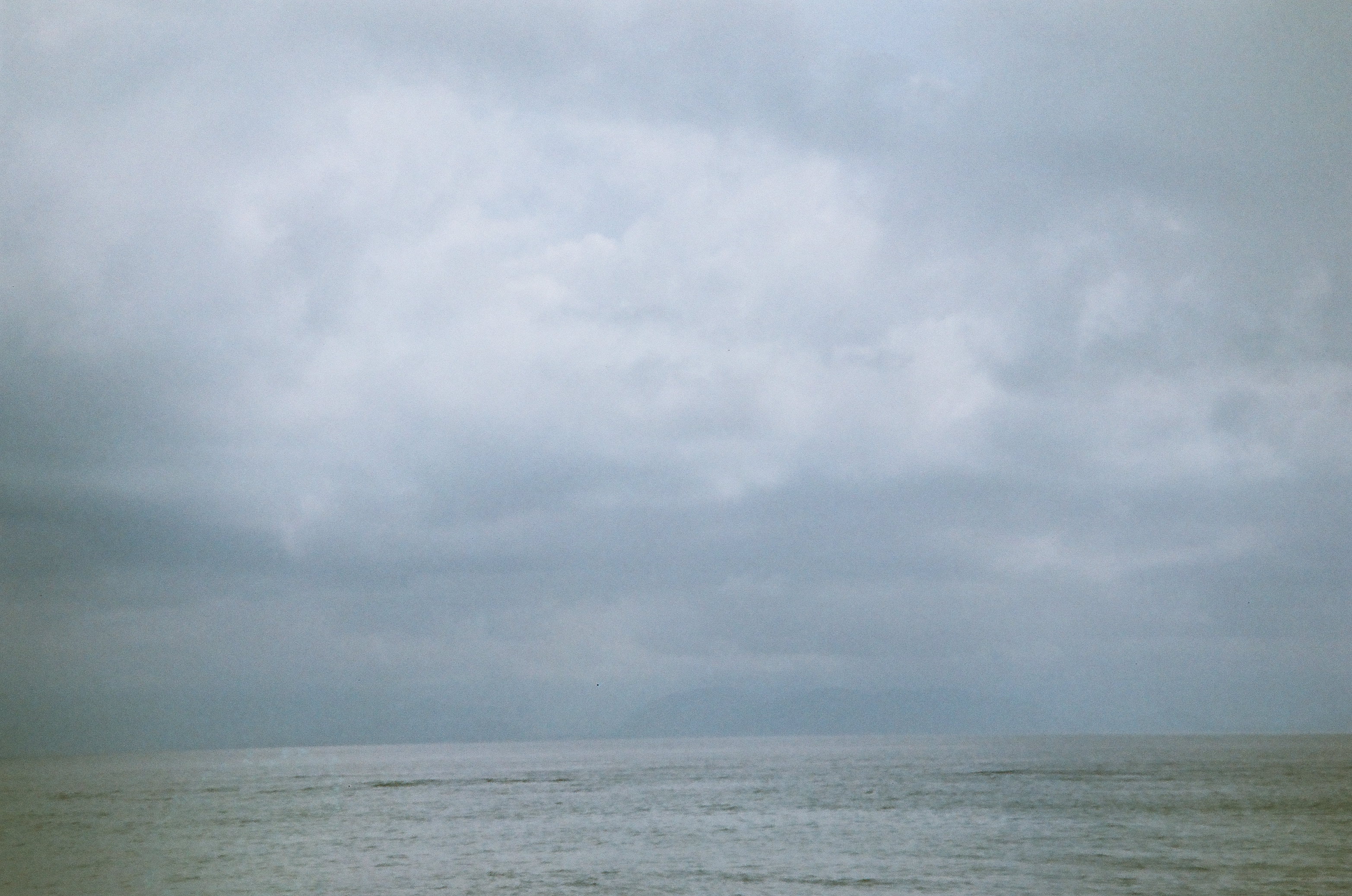 Layered gray clouds fill the sky above open water, separated by a faint, nearly level horizon.