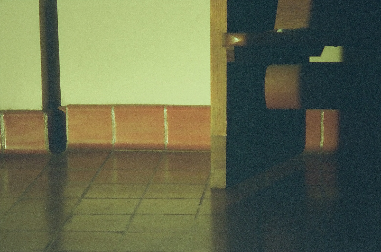 Tall narrow shadows from a lectern and wall edges extend across glossy terracotta tiles in a pale interior.