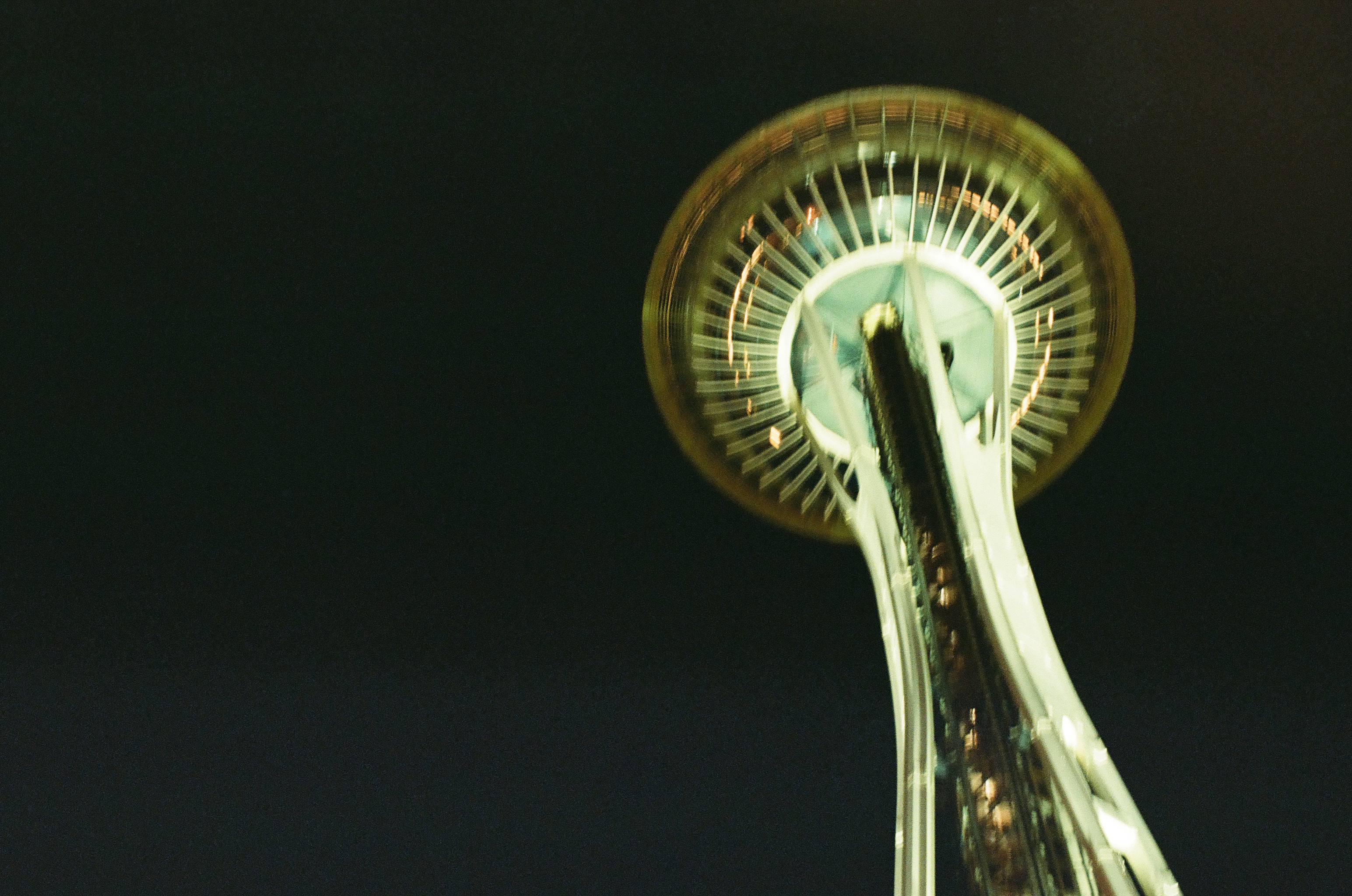 A bright divided column rises into a green-white circular top edged by amber arcs against deep darkness.