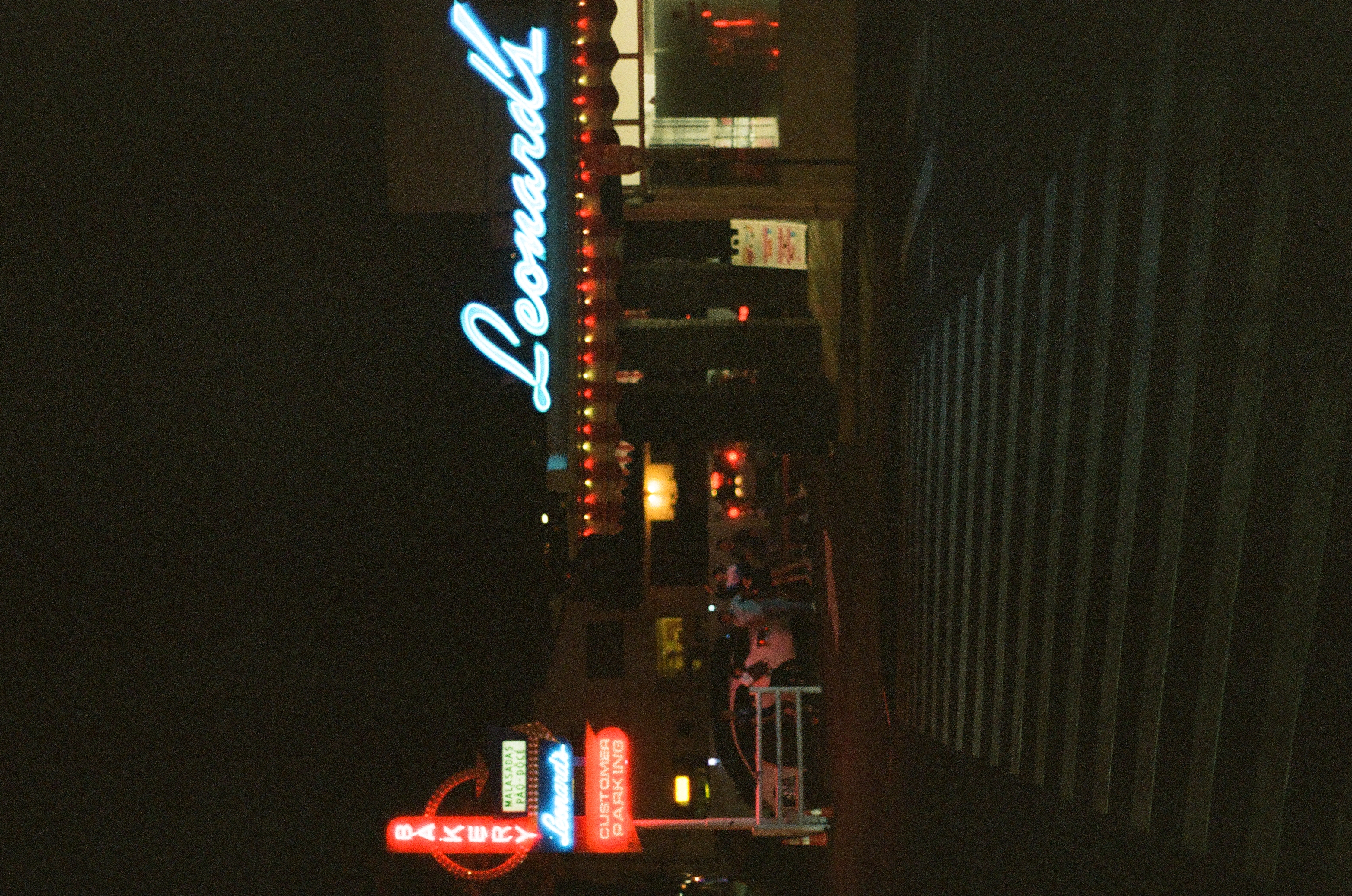 Leonard's neon sign glows above a dark restaurant exterior beyond a striped crosswalk at night.