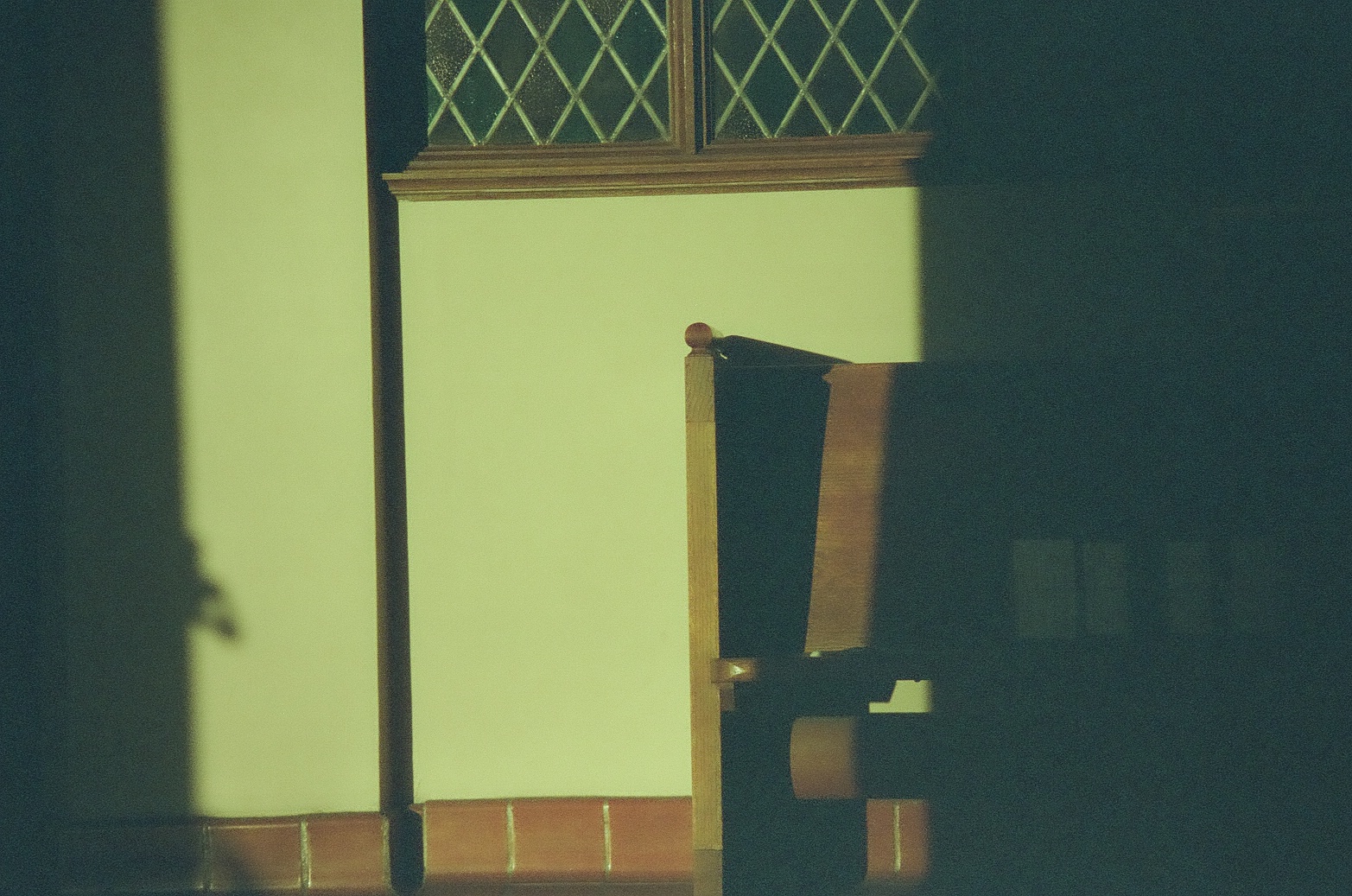 A wooden chair at the frame edge casts a broad dark silhouette across warm tiles and a pale wall.