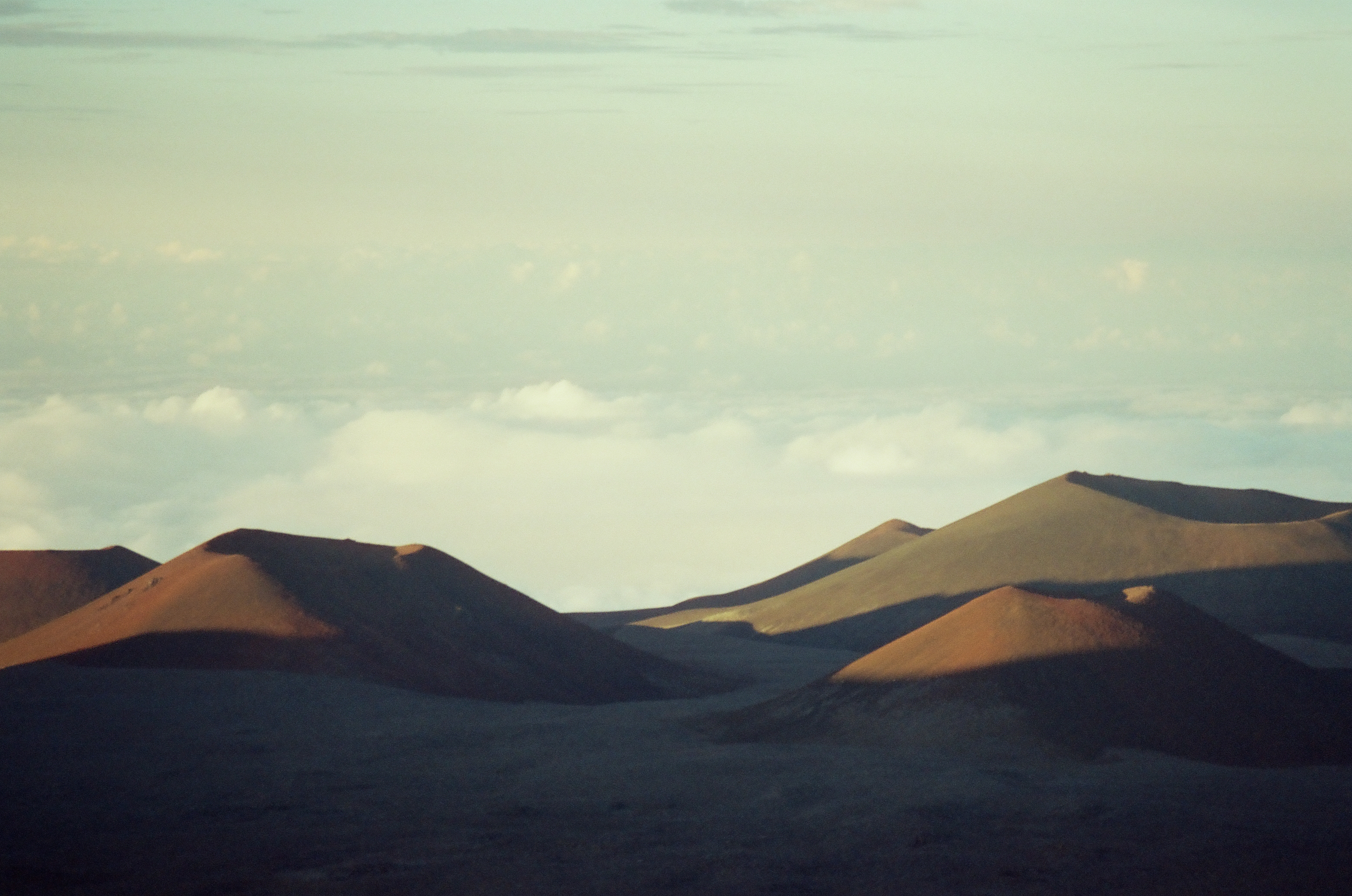 Warm light crosses several rounded brown slopes while broad cool shadows pool between them.