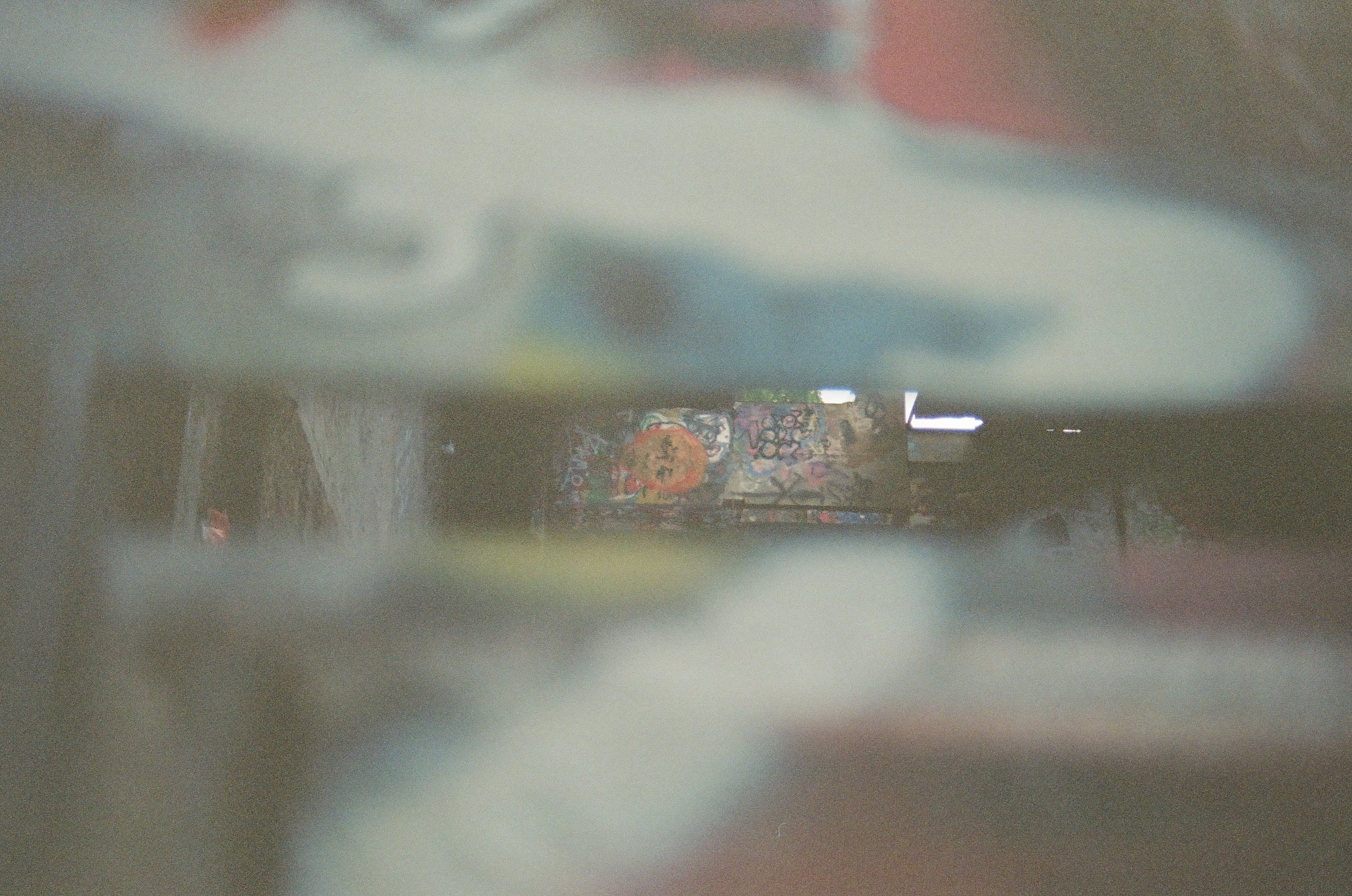 Blurred foreground shapes frame a narrow view into a dark, graffiti-covered corridor with an orange circular design partway down the passage.