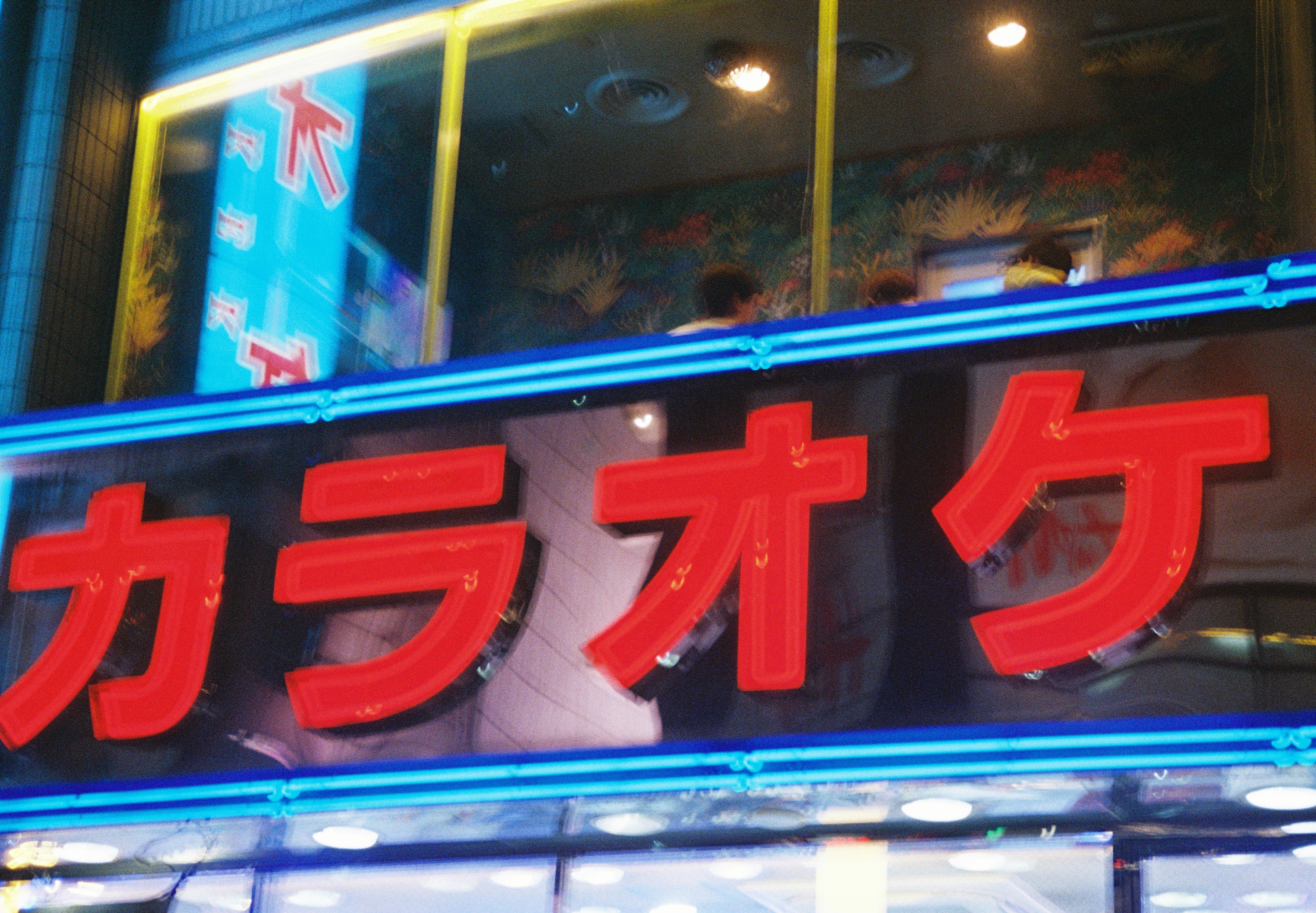 Large red neon characters spelling 'karaoke' in katakana glow above a storefront edged with blue neon tubing.