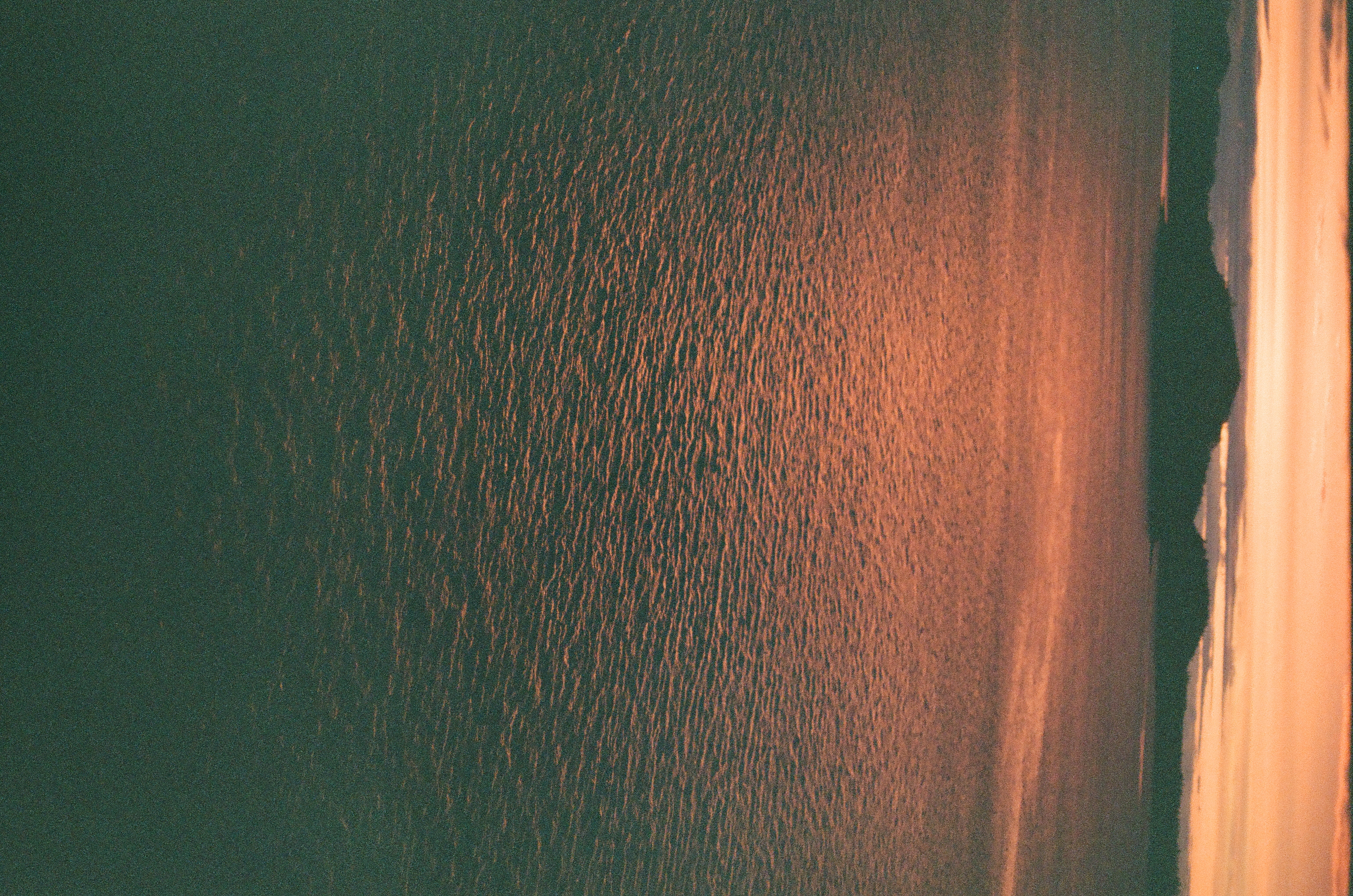 Rippling water fills a vertical view beneath a peach horizon and several distant dark islands.