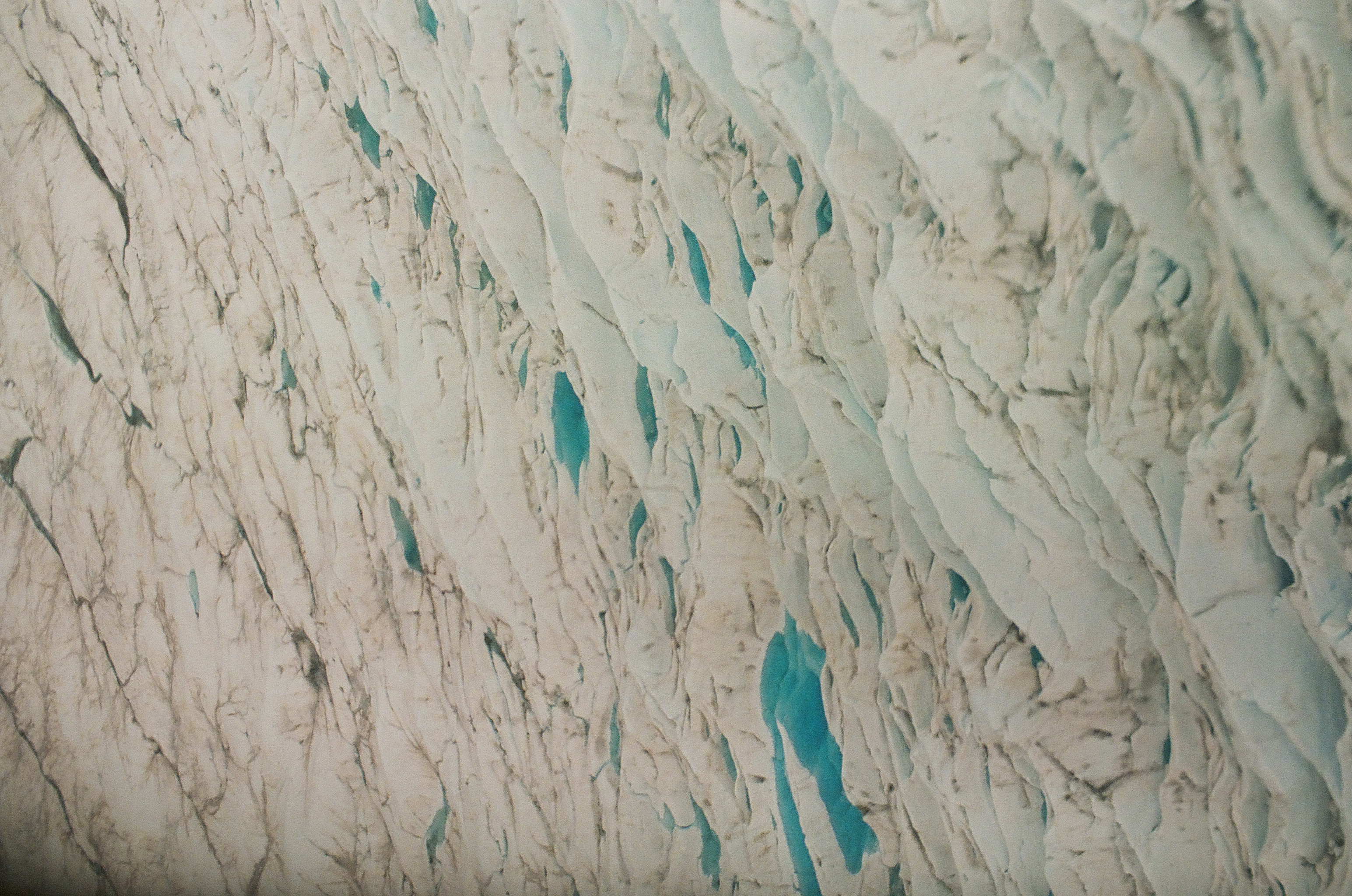 Turquoise pools and narrow blue seams punctuate a wide field of cracked gray-white glacier ice.