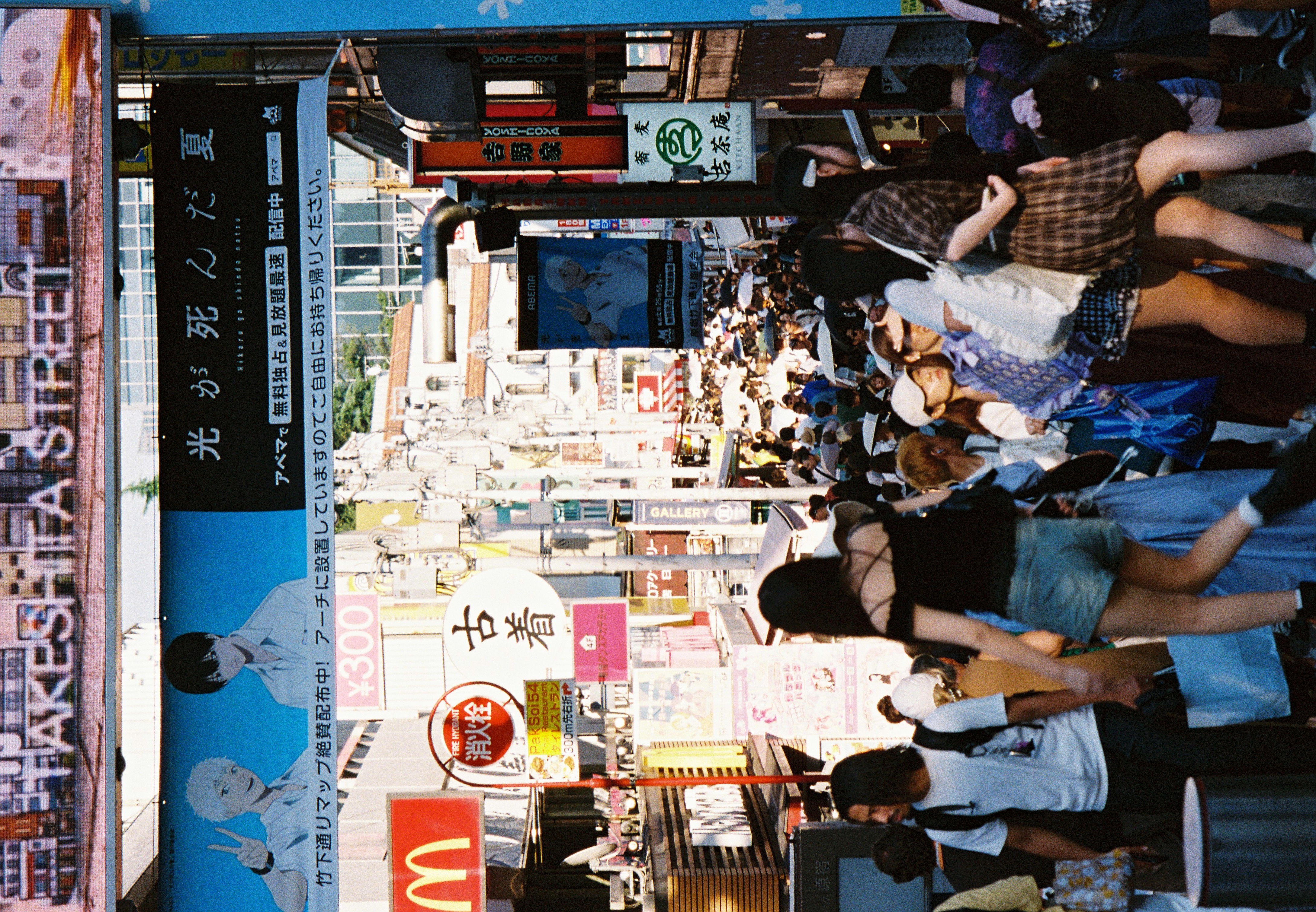 A digital marquee reading TAKESHITA STREET tops an illustrated billboard as pedestrians cross beneath it into a densely signed, crowded lane.