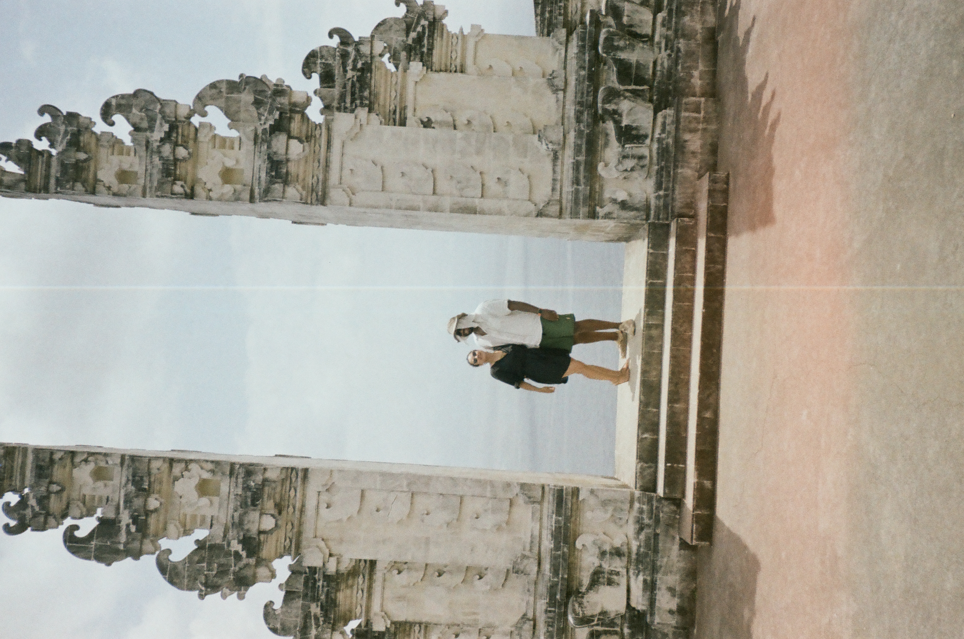 Two people stand close together above three steps between carved towers, with a pale vertical line near the center.