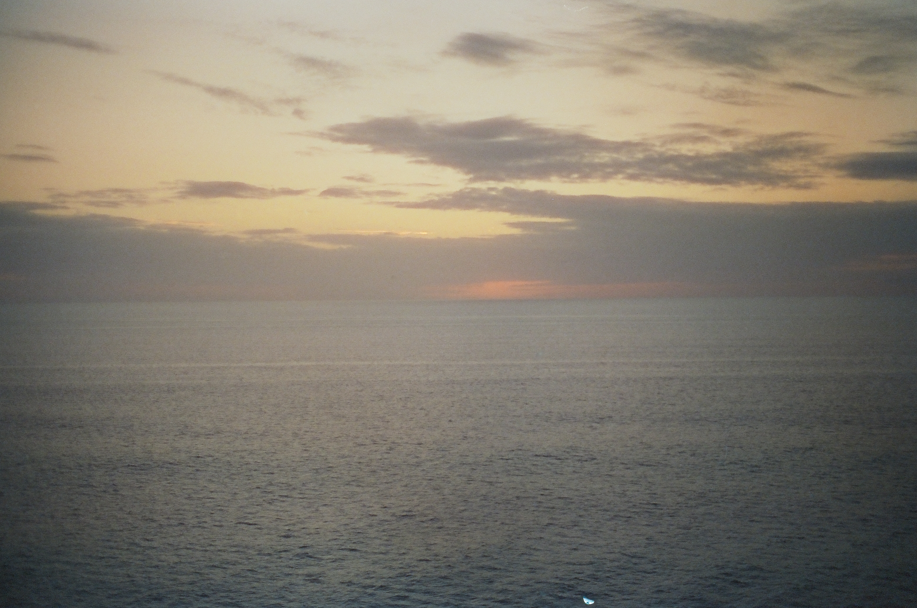 An amber band of light glows along the sea horizon beneath gray clouds, with dark finely rippled water below and no sun visible.