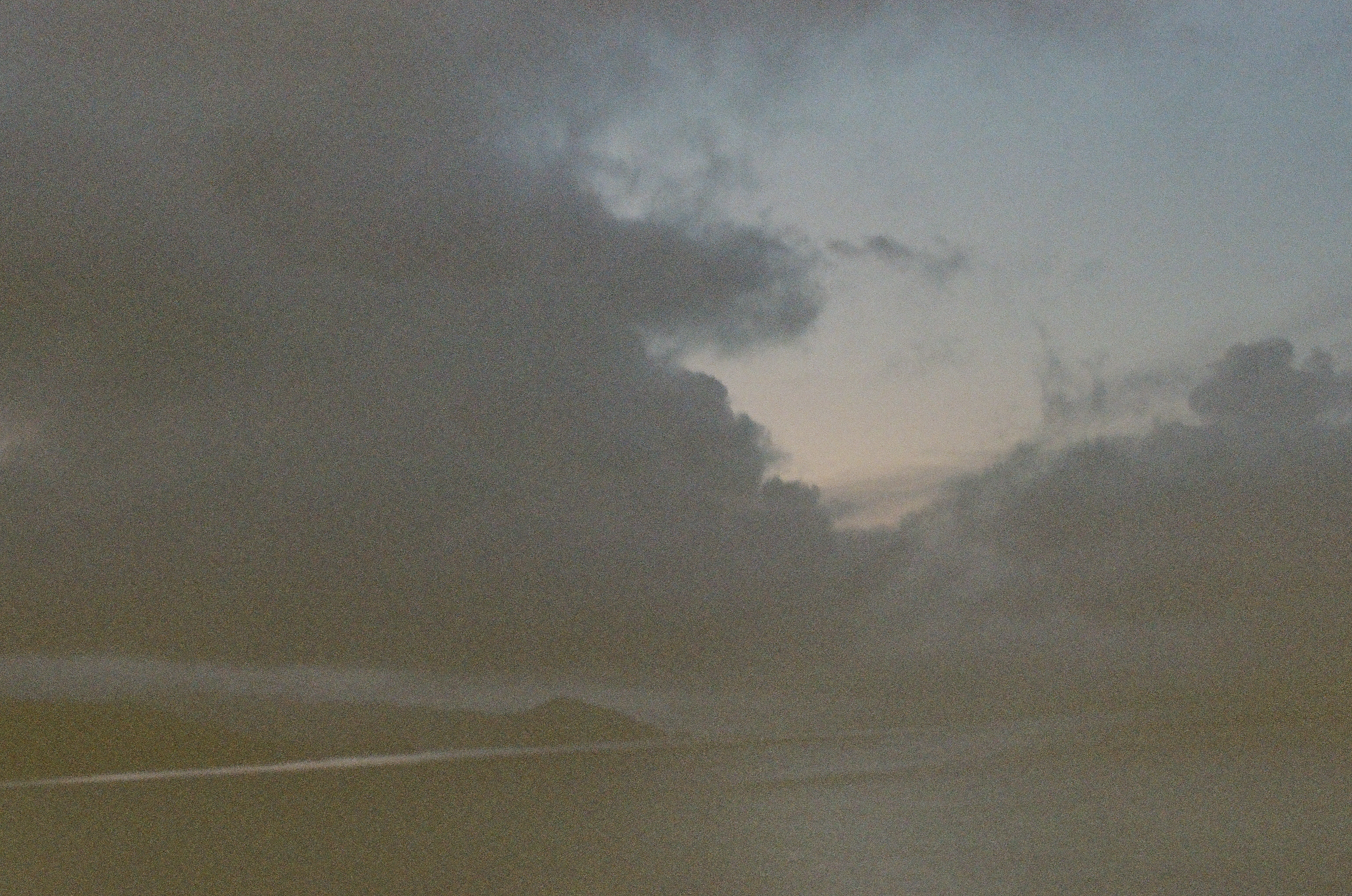 Layered storm clouds open slightly above a chain of low dark ridges stretching across calm water.