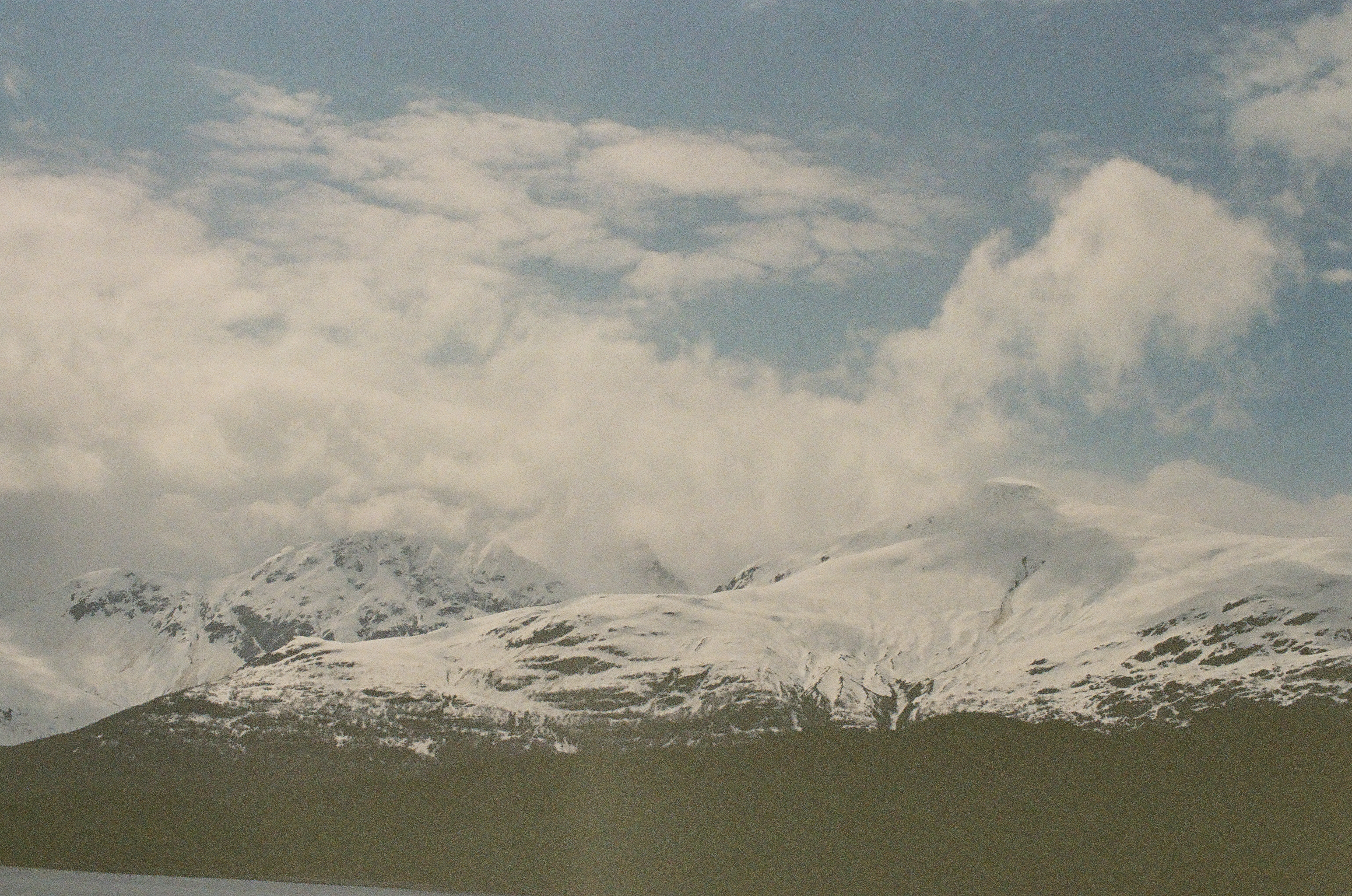 A broad snow-covered mountain range stretches above dark water while low clouds cross the highest ridges.