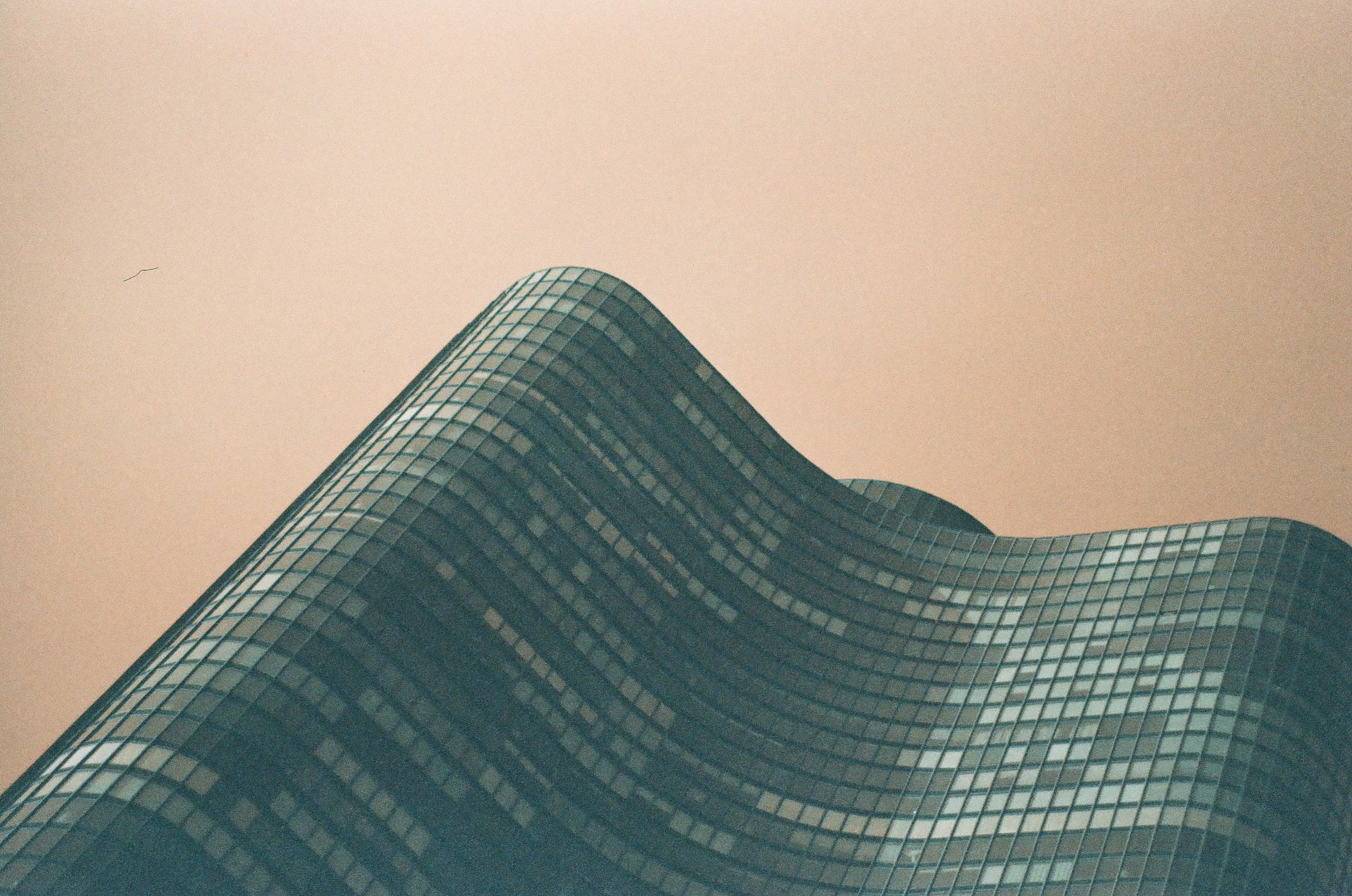 Two rounded peaks of a wave-shaped glass facade fill the frame, their mirrored panels catching light against a warm blank sky.