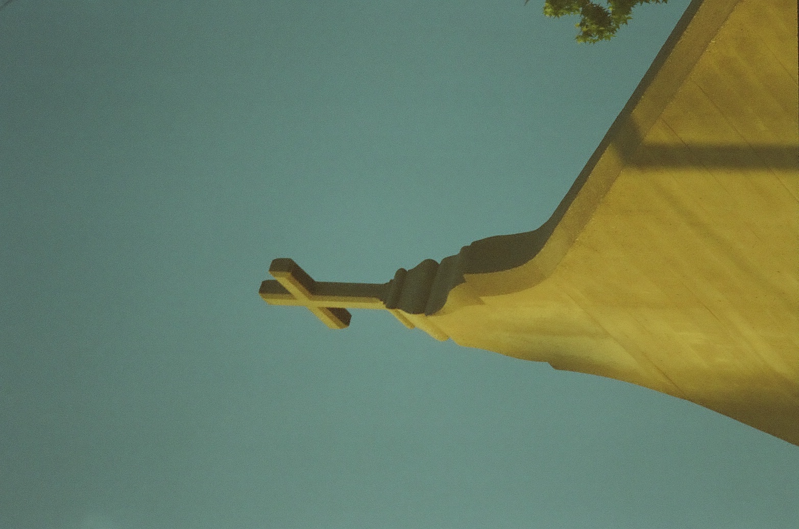 A small cross crowns a steep pale wall glowing golden against an open blue-green sky.