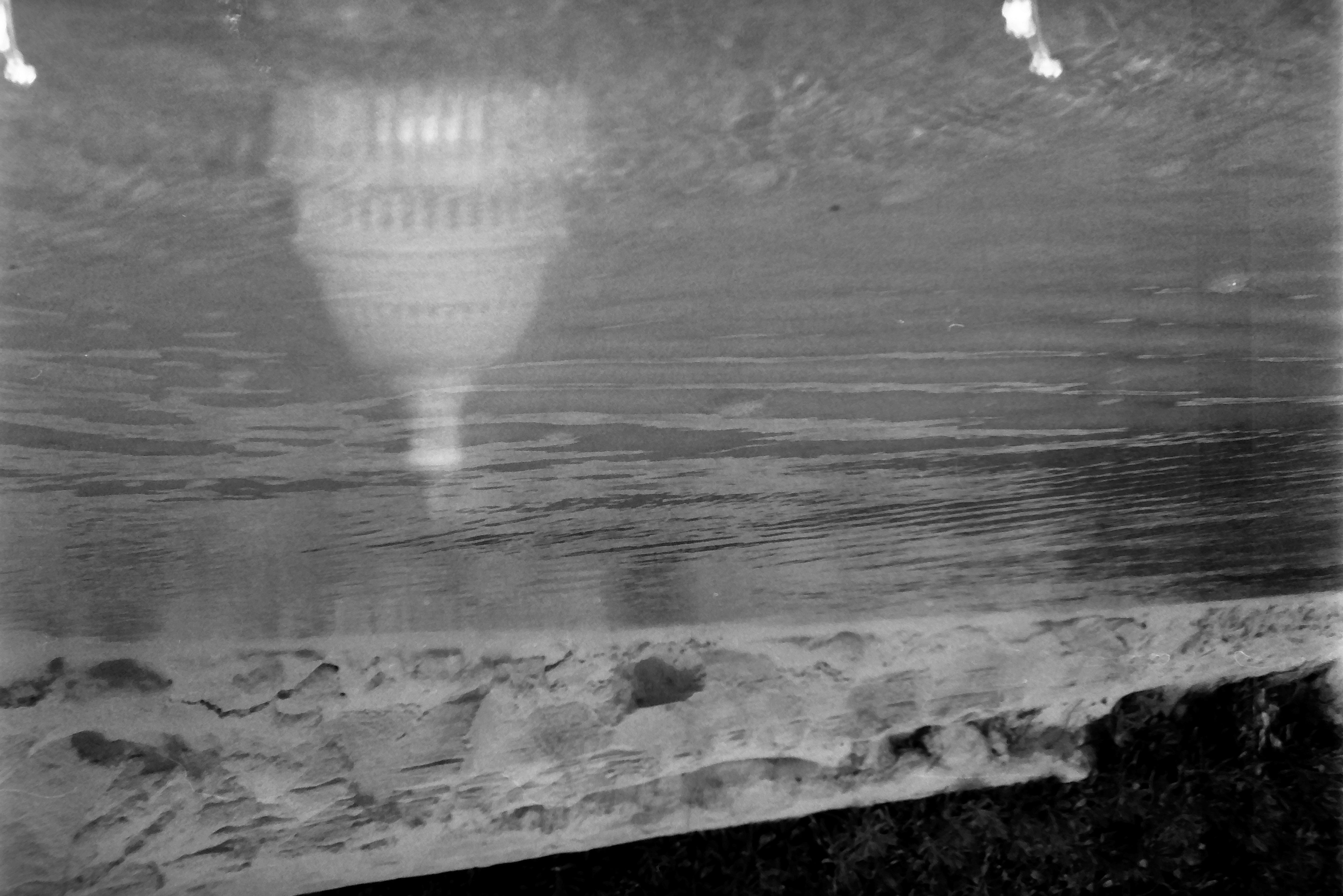 Rippled shallow water spreads below a pale rocky bank, while a faint ribbed dome with a columned base appears in the lower right.