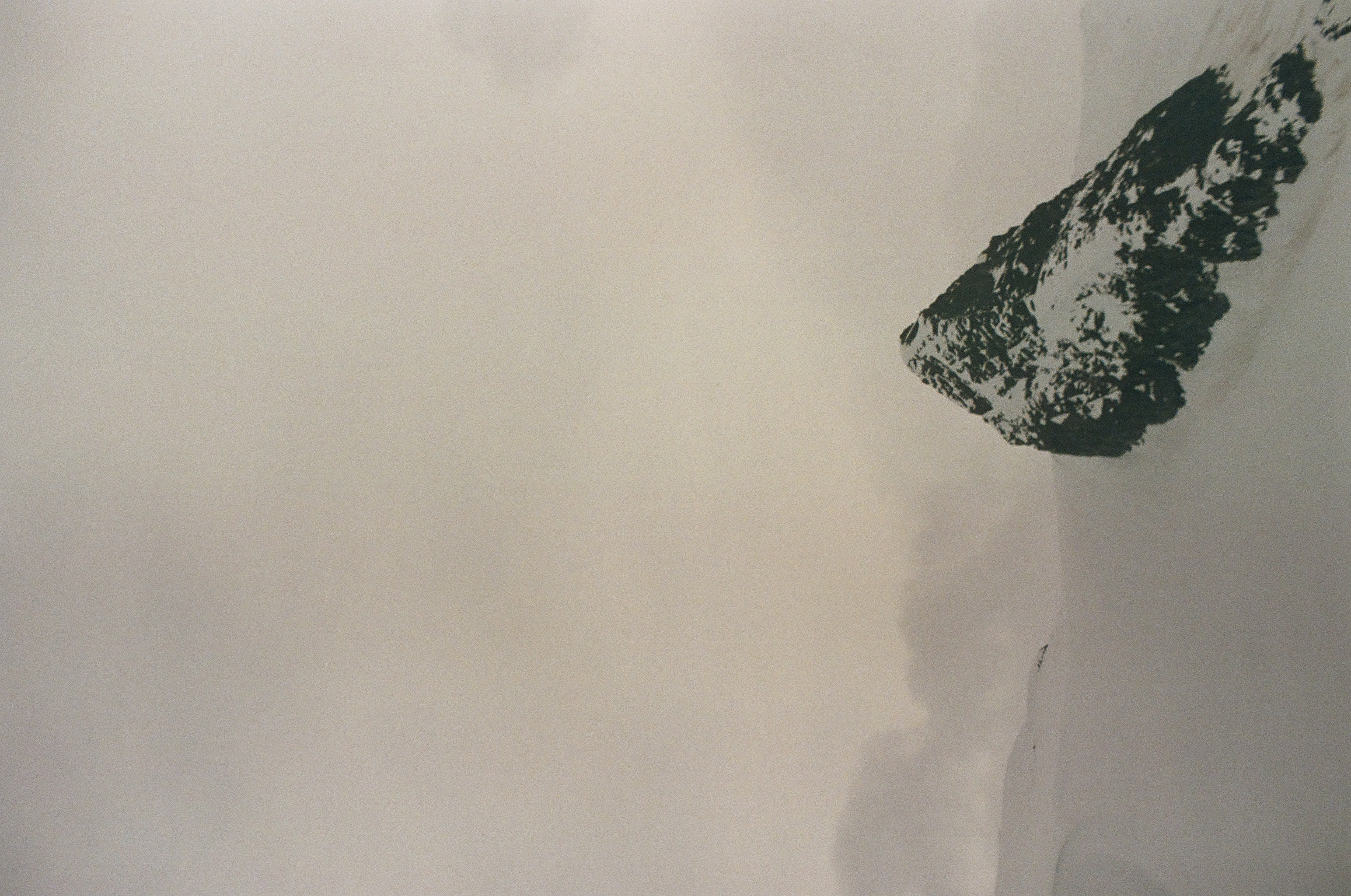 A single dark triangular peak emerges from white mist with only a faint snowy shoulder nearby.