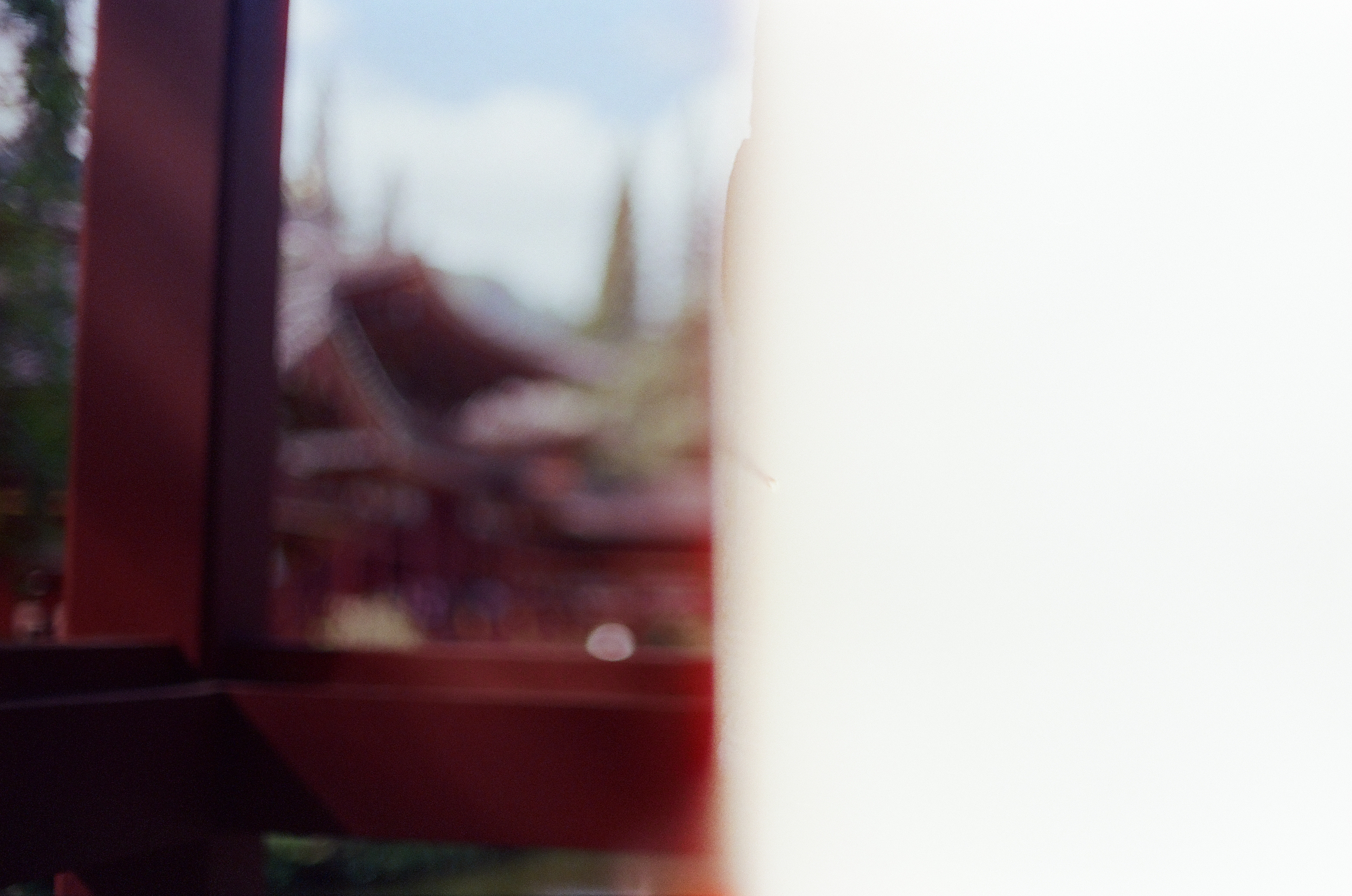 An overexposed frame dissolves into white and red light, leaving only a faint blurred silhouette of a curved temple roofline at the far left.