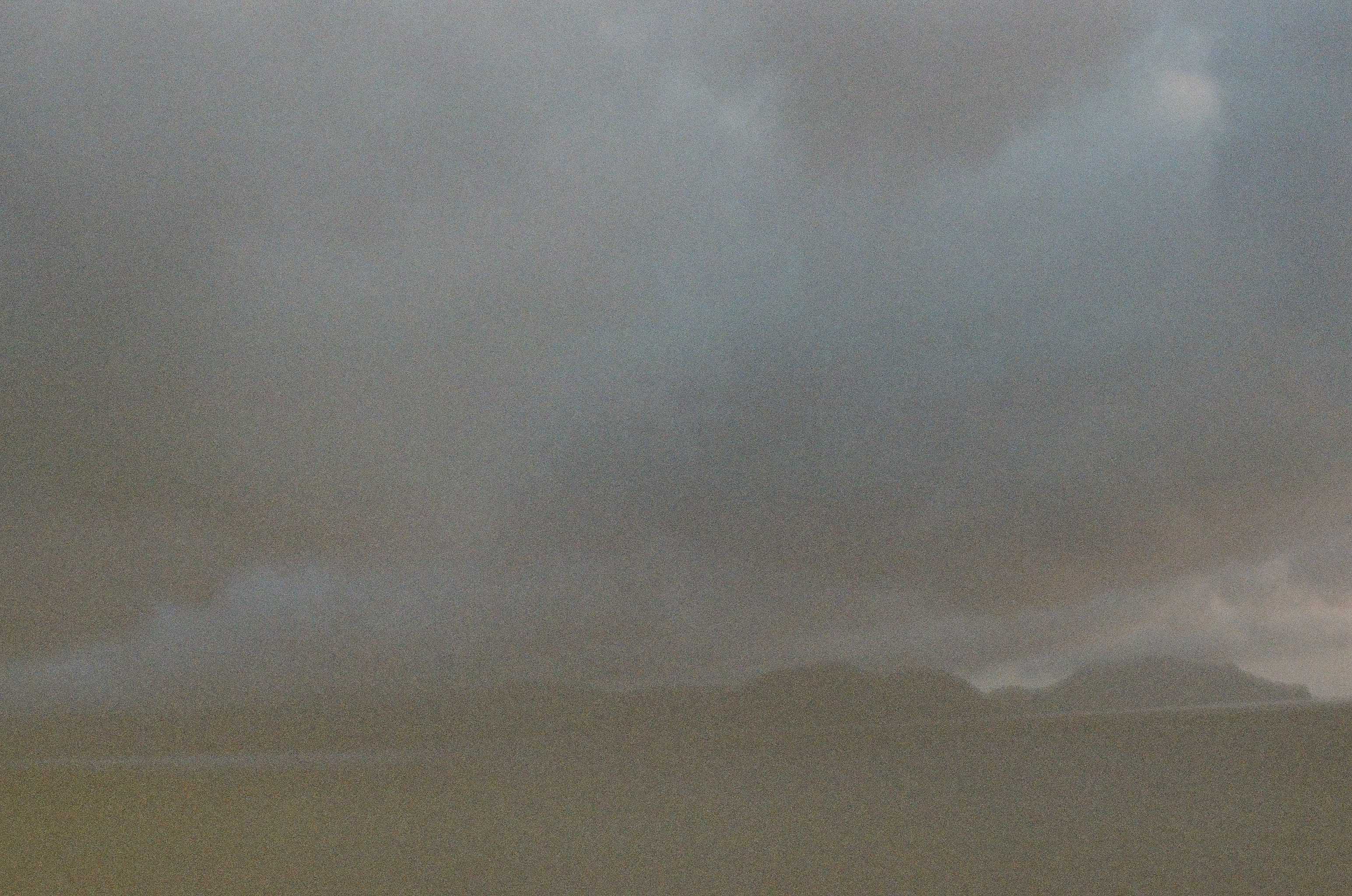 A broad gray cloud bank hangs above dark island silhouettes and a nearly black strip of water.