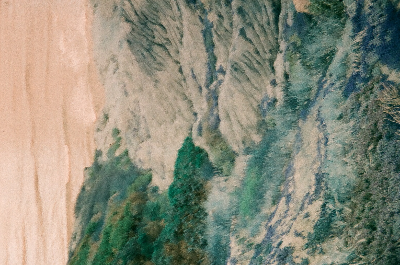 Layered rounded rock fills a narrow coastal view beneath pale water and a warm color-shifted sky.