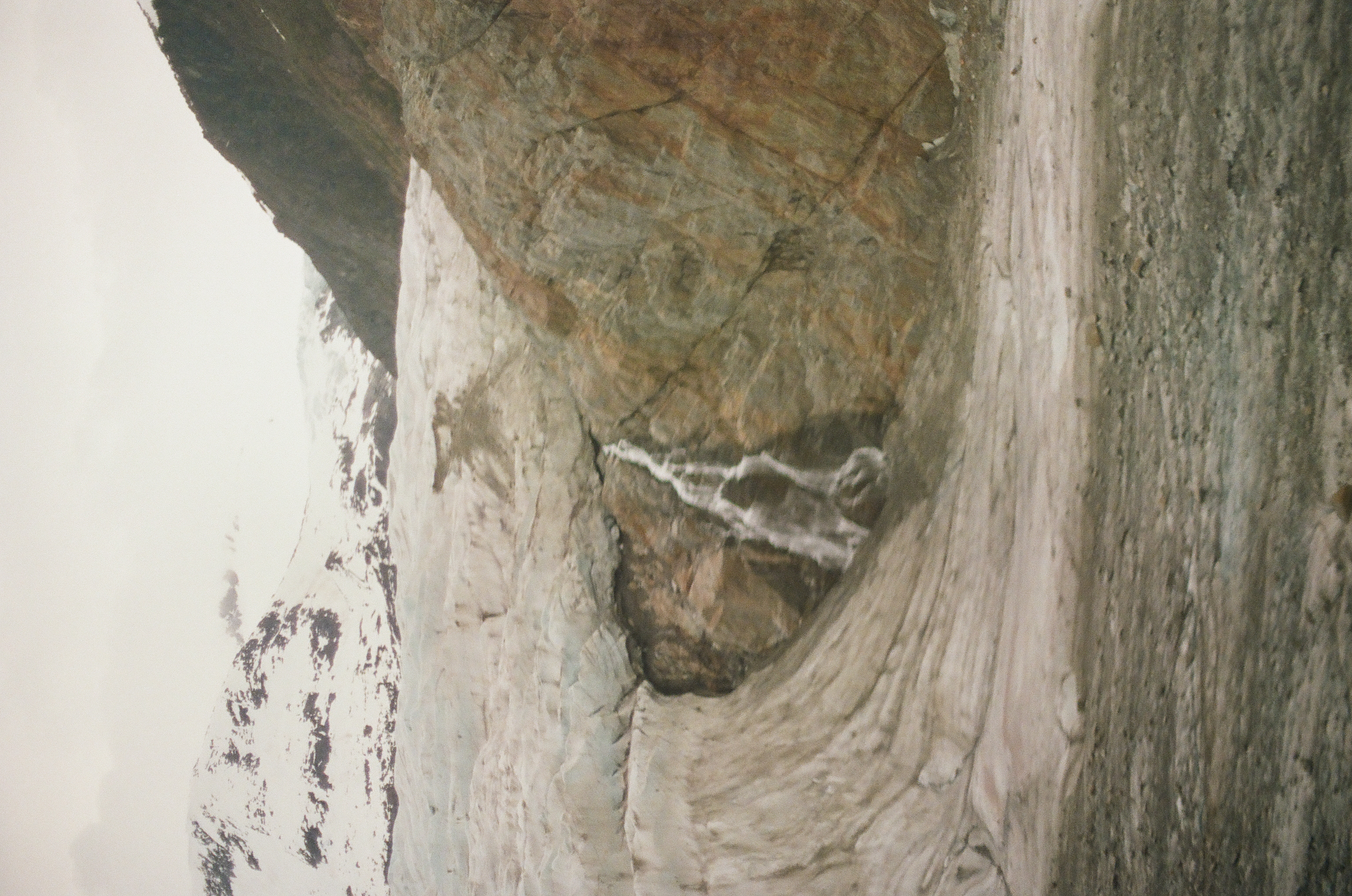 A narrow waterfall drops across rust-colored rock beside dirty snow and a receding glacier.