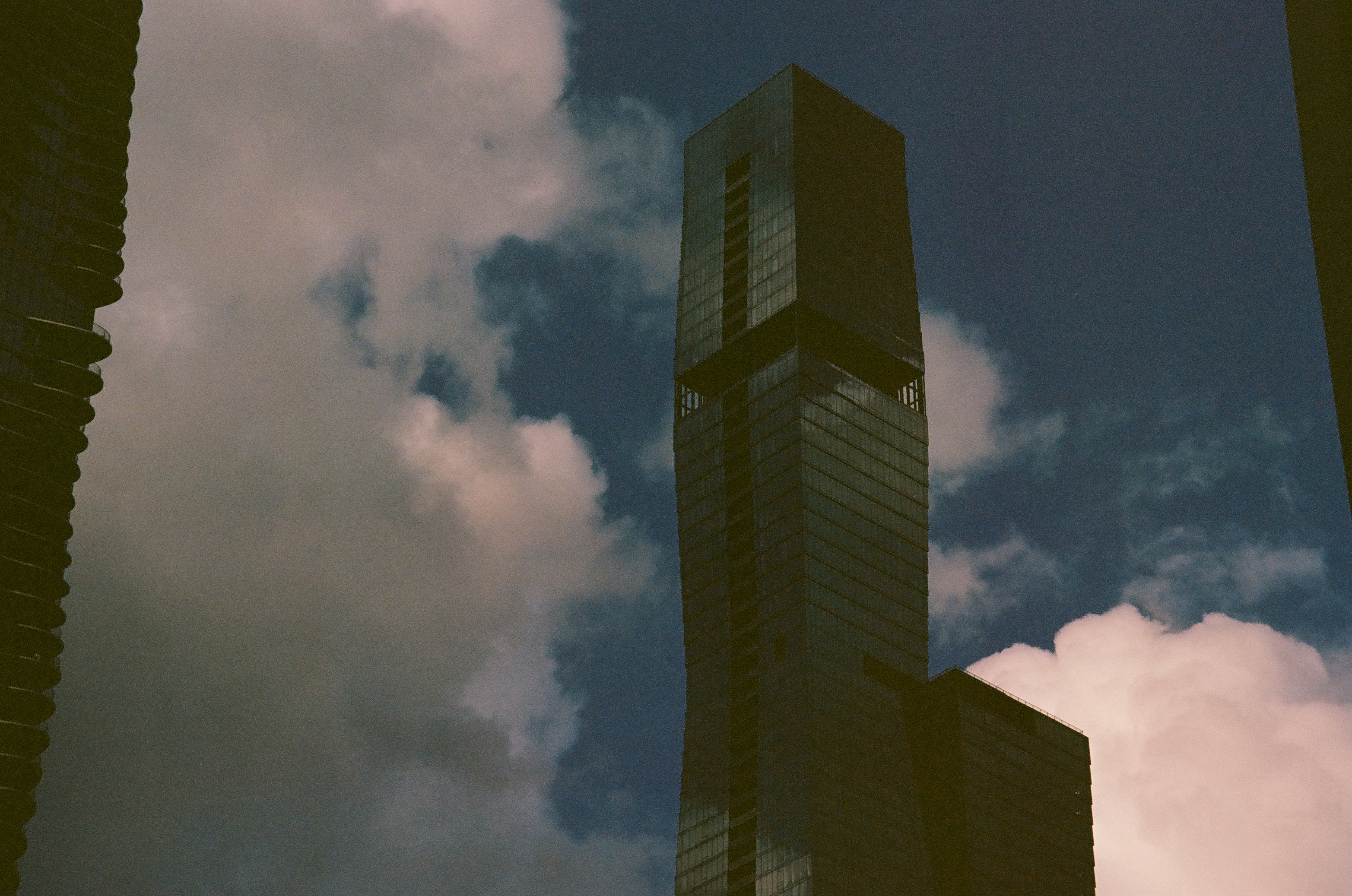A tall rectangular tower stands between neighboring walls against blue sky and soft white clouds.