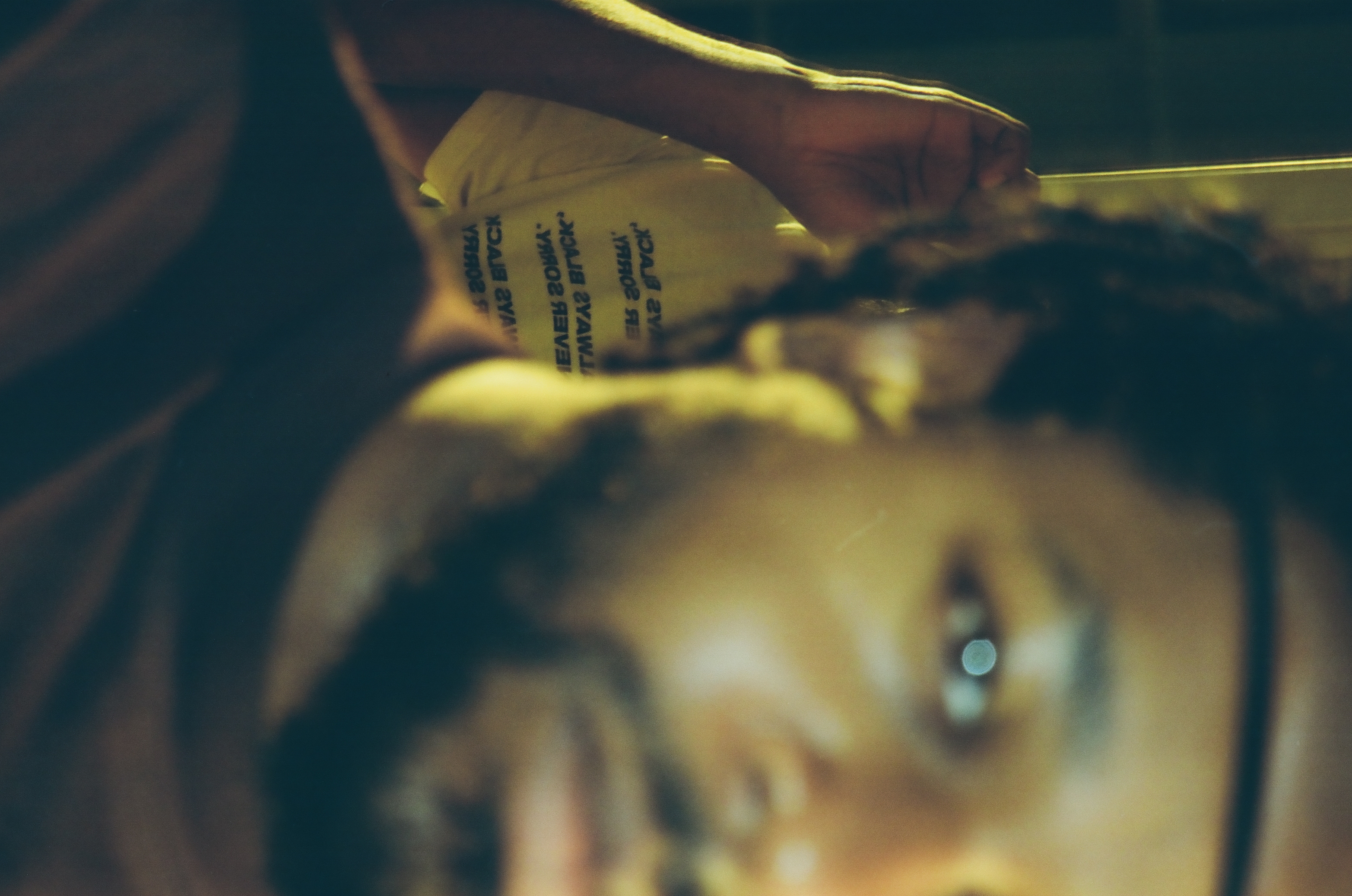 A hand holds a folded printed flyer close to the lens, its mirrored text overlapping a blurred, warmly lit face behind it.