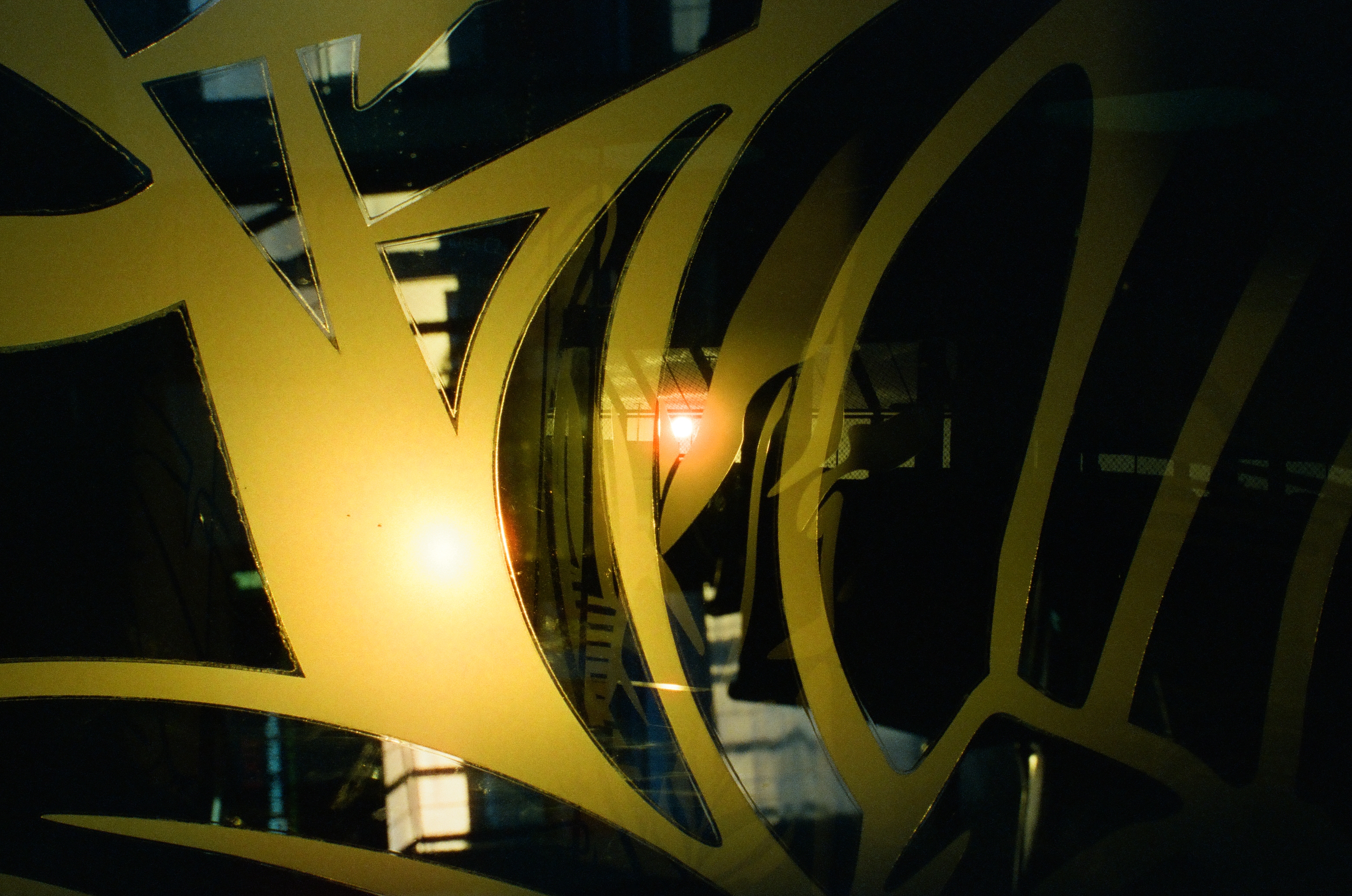 Glossy yellow and black curved shapes overlap with layered reflections and a small red light.