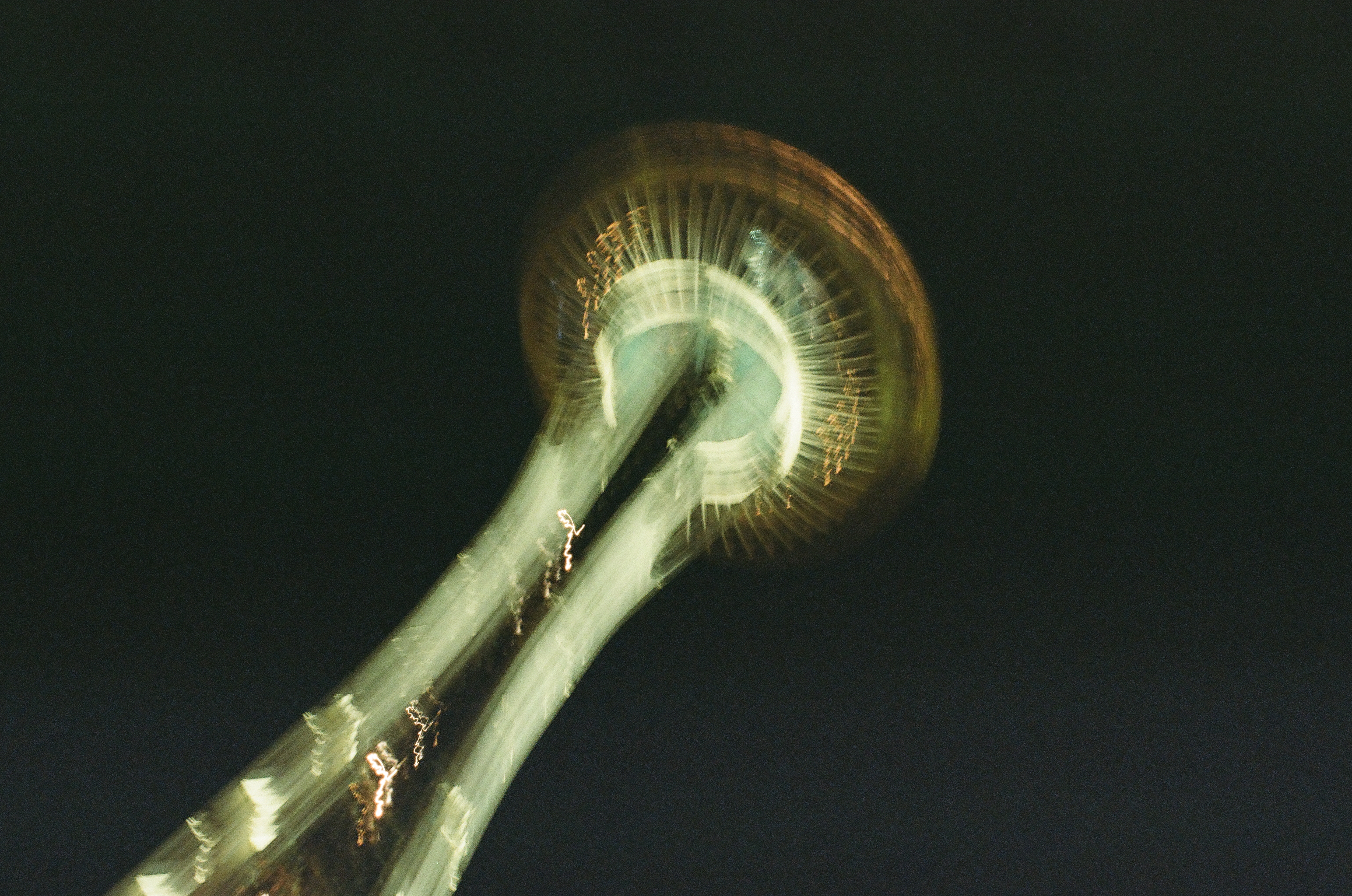 Two broad pale bands angle toward a blurred green-white circular crown with amber marks against a black sky.