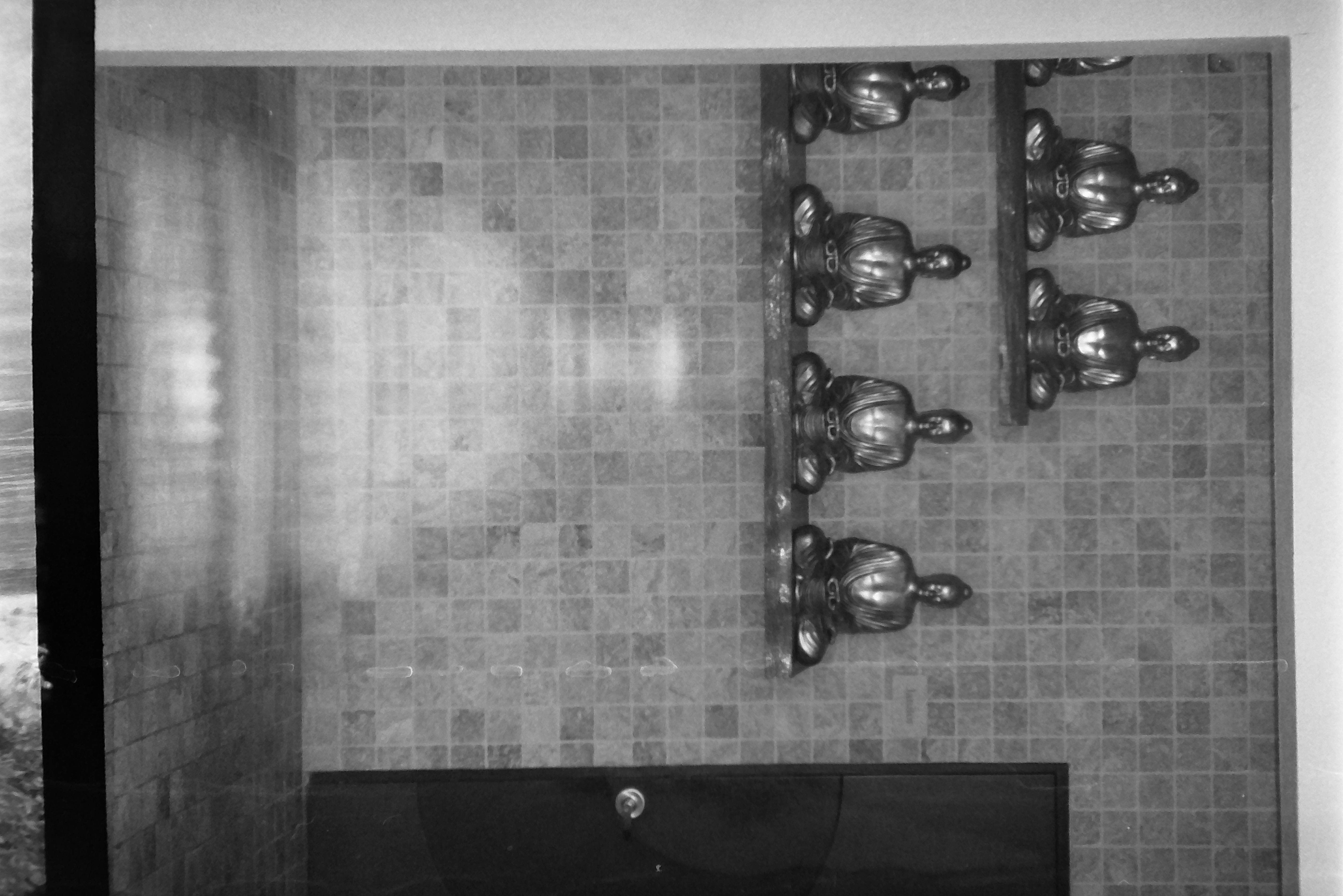 Seven small seated figures rest on two shelves against a wall of small square tiles, beside a dark door with a round knob.