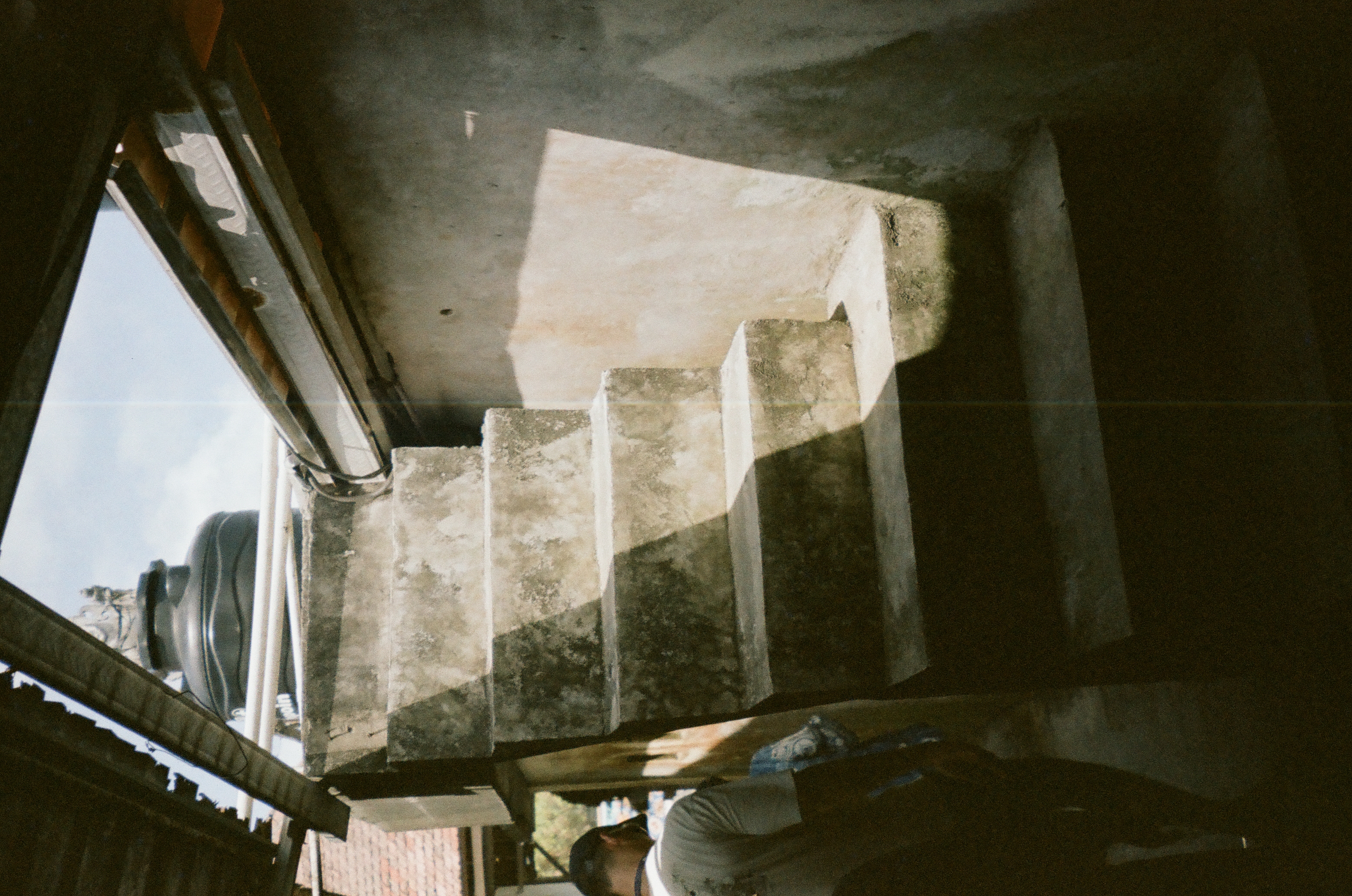 Thick concrete steps rise between a sunlit wall, deep shadow, pipes, and a dark tank.