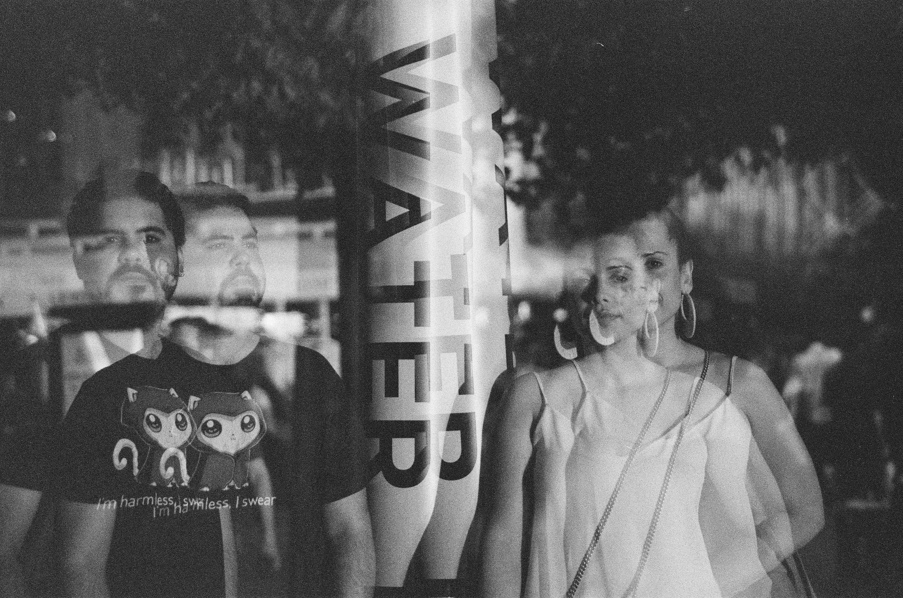 A woman at right remains clear while a man’s face and torso repeat faintly across the center of the monochrome frame.